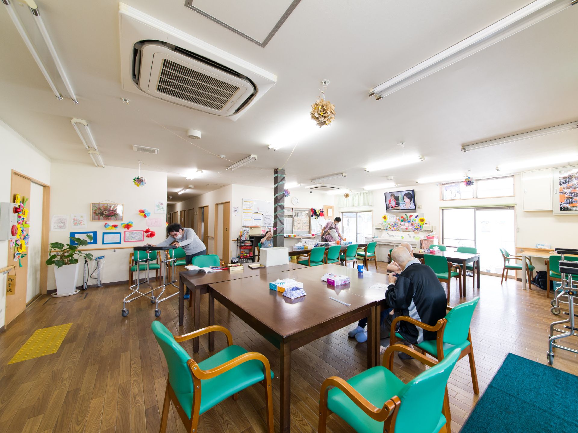 多目的ホールでは、食事時以外にも入居者達が自由に過ごしている。歩行器で運動する人や、座って談笑する人たちがいる。