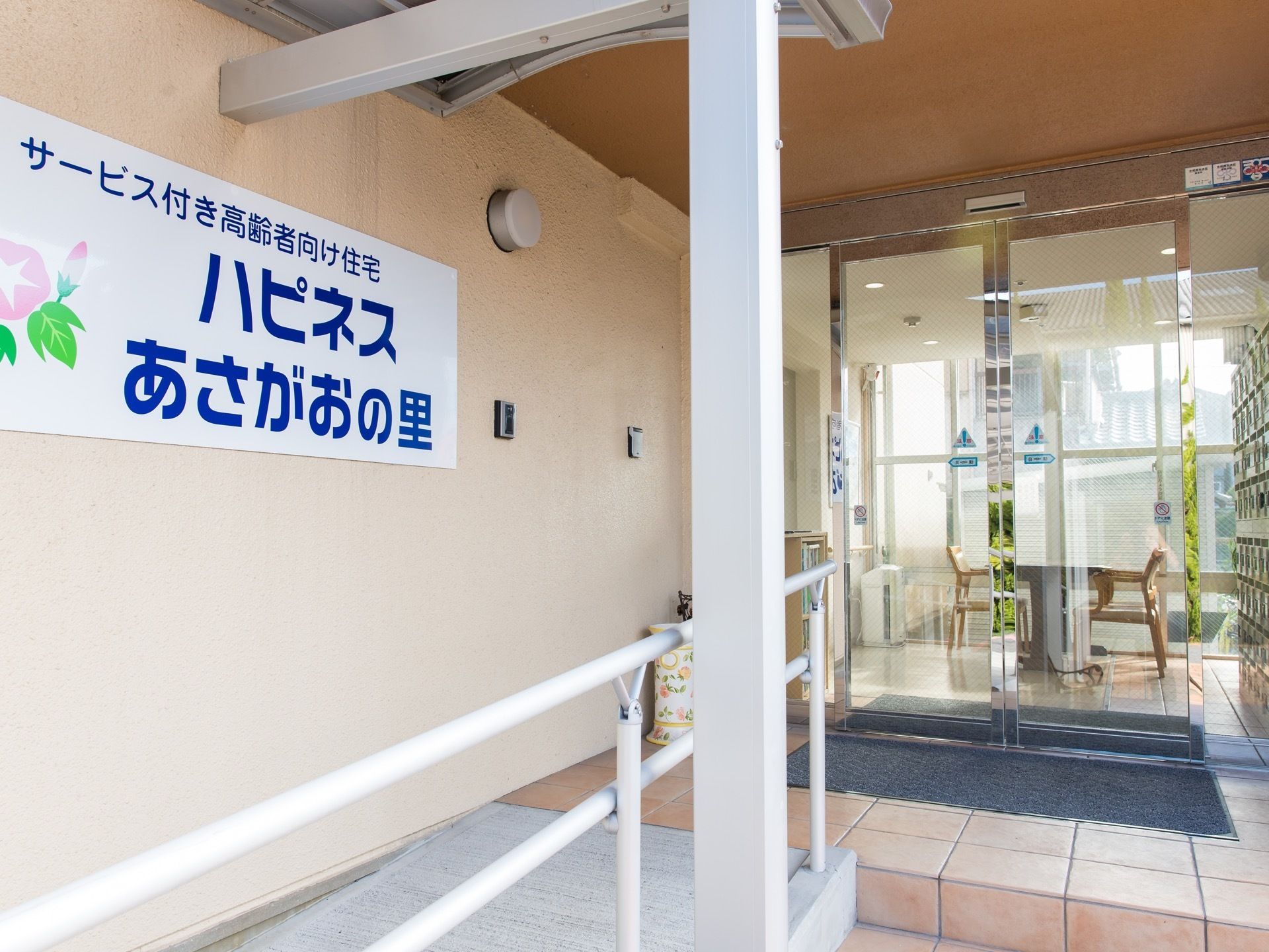 ガラス製の自動ドアの玄関となっている。入り口の外の壁には、施設名が書かれたプレートが取り付けられている。
