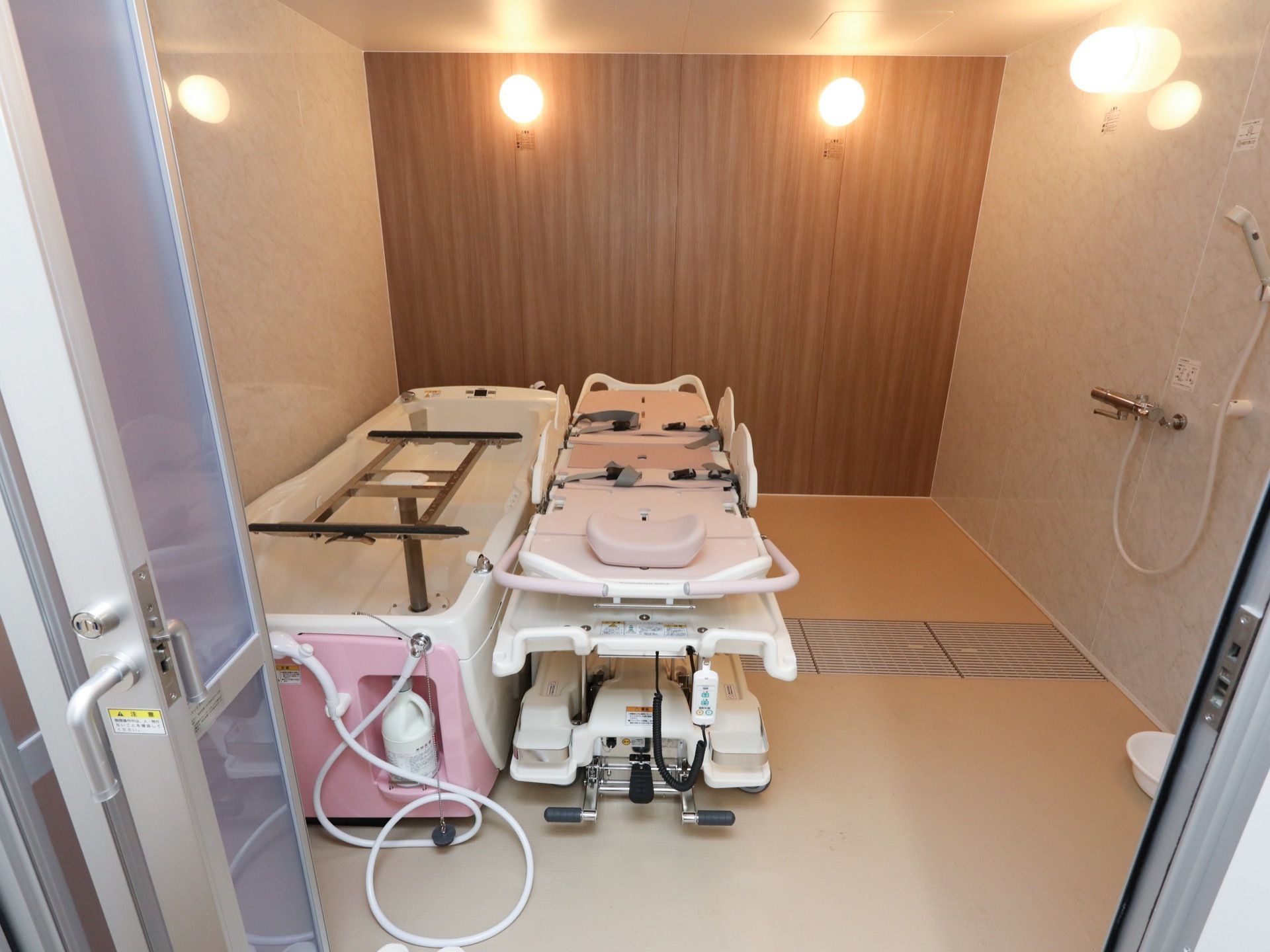 木目調や模様入りの３種の壁に囲まれた浴室に、機械浴のシステムが備えられている。横になった状態で入浴することが可能。