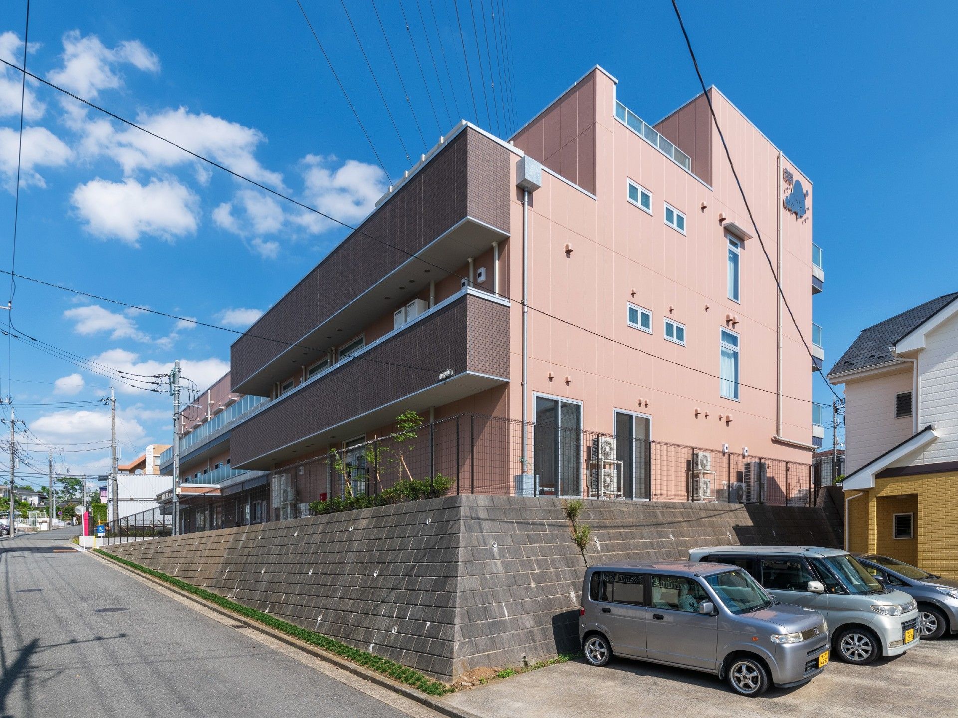 3階建ての建物を左手前から見た様子。建物の周りには黒いフェンスがある。