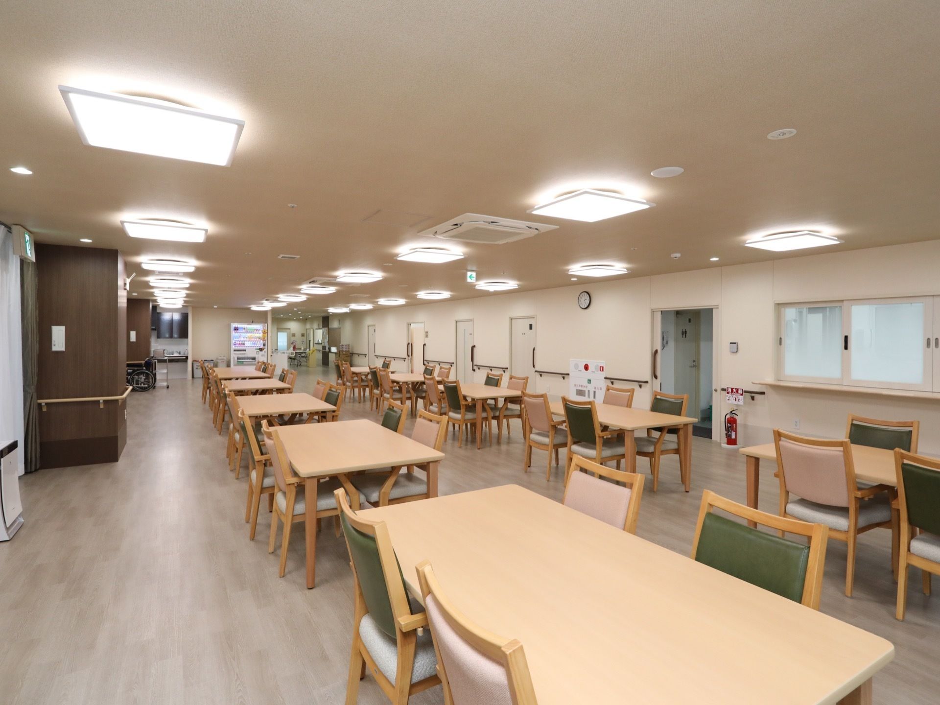居室前に設けられている食堂で、奥には自動販売機が設置されてる。天井には複数の照明が取り付けられており、明るい。
