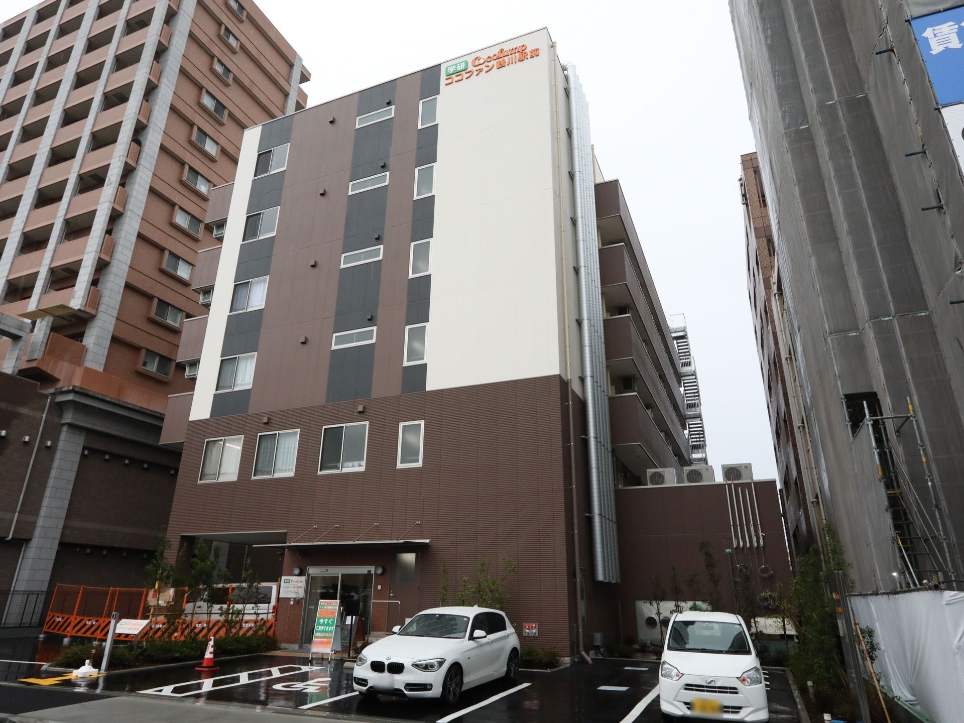 住宅街の中にある６階建ての大きな建物で、周辺には複数のマンションが建てられている。上部の壁には、施設名が書かれている。