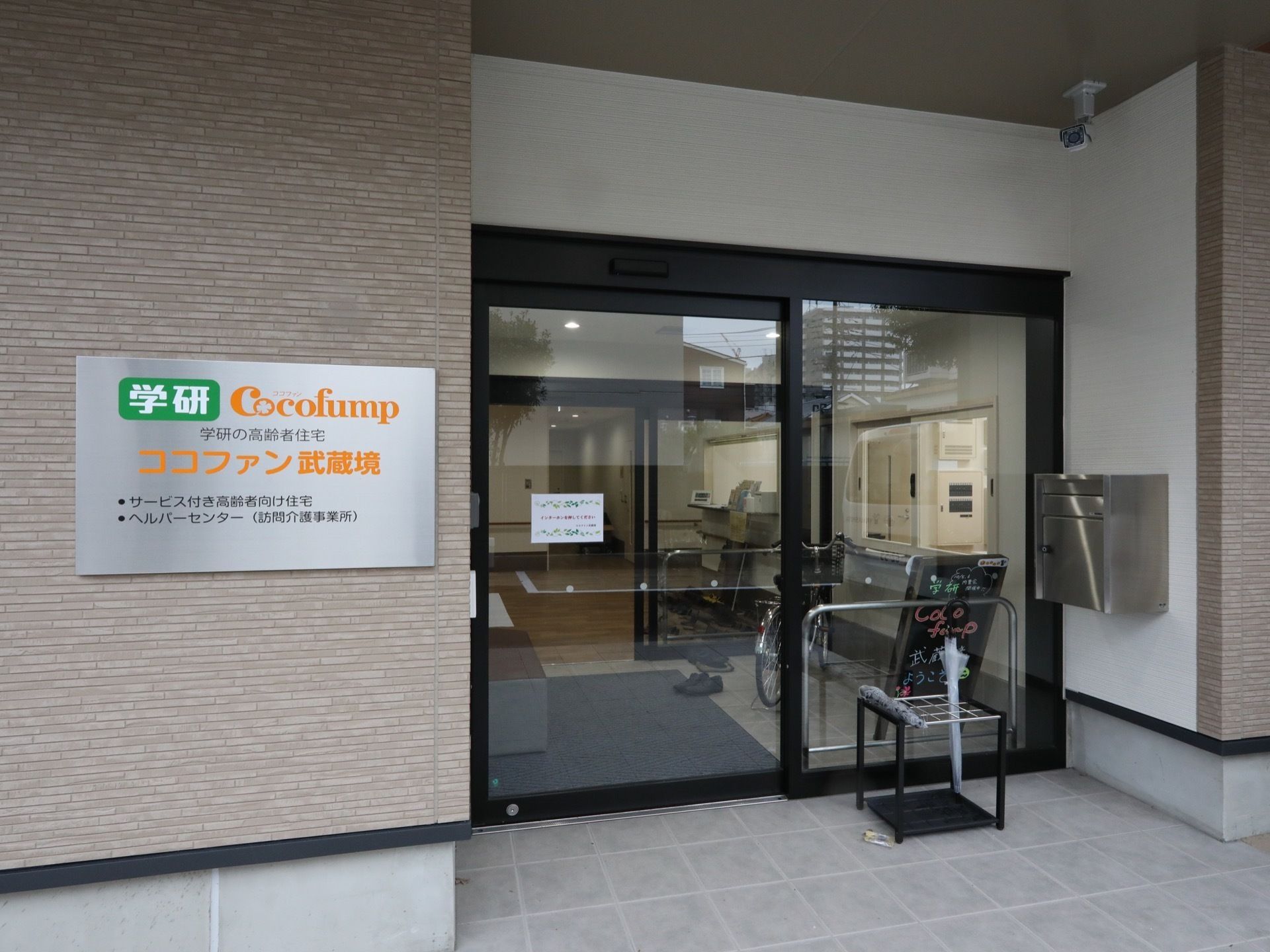 ガラス張りの自動ドアが設置されている玄関。横には、郵便ポストや施設名が書かれた表札が取り付けられている。