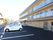 施設の建物と隣接する駐車場に数台の車両が停まっている。スペースは白線で仕切られ、車止めも設置されている。