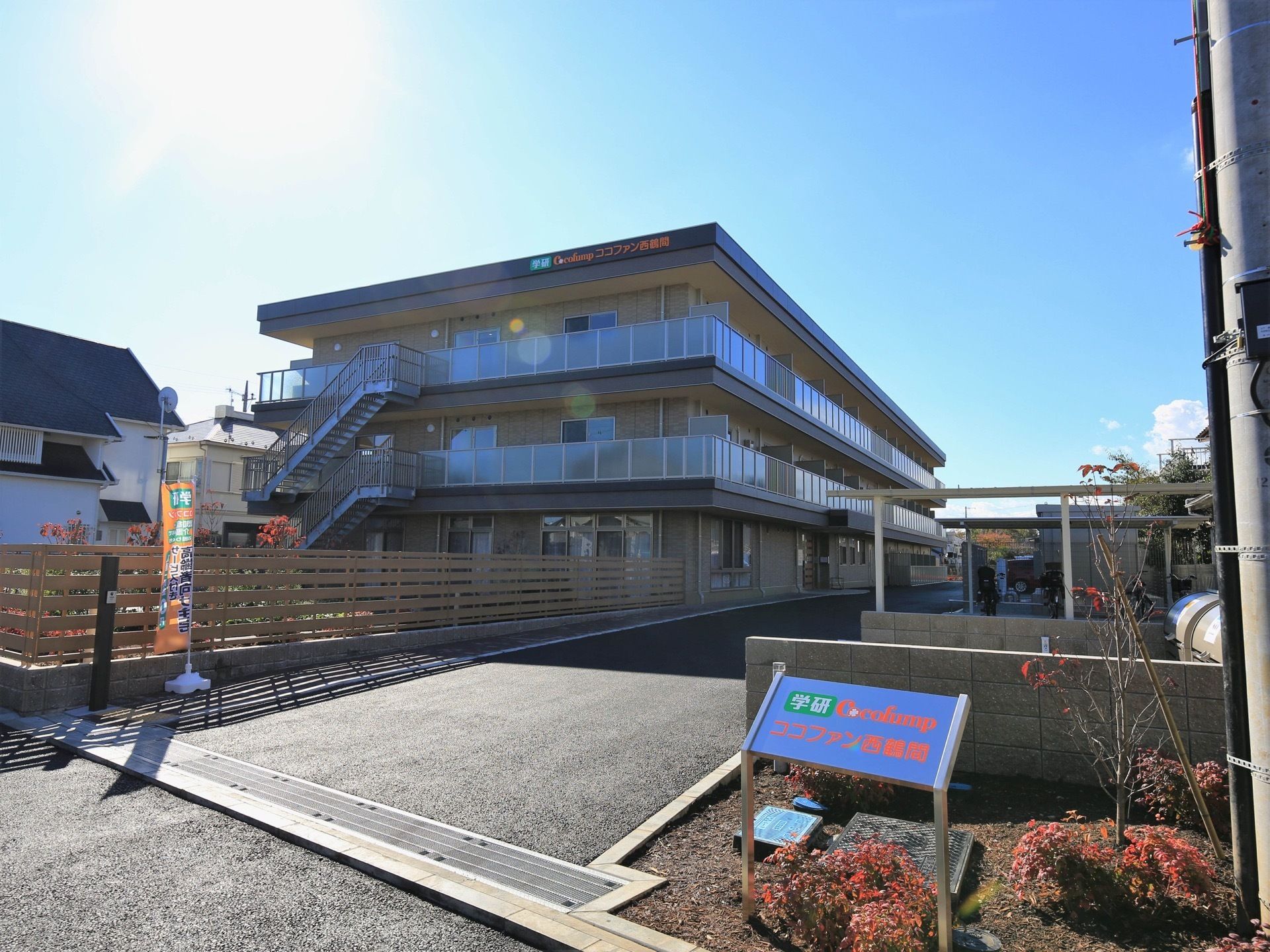 看板が手前にあり、奥には３階建ての建物がある。敷地の入口はスペースにゆとりがあり、車両が進入しやすい。