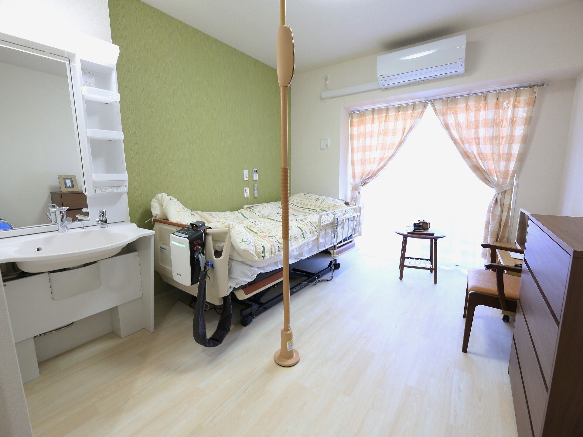 洗面台と介護用ベッド、つかまり棒が設置され、緑の壁が可愛い居室