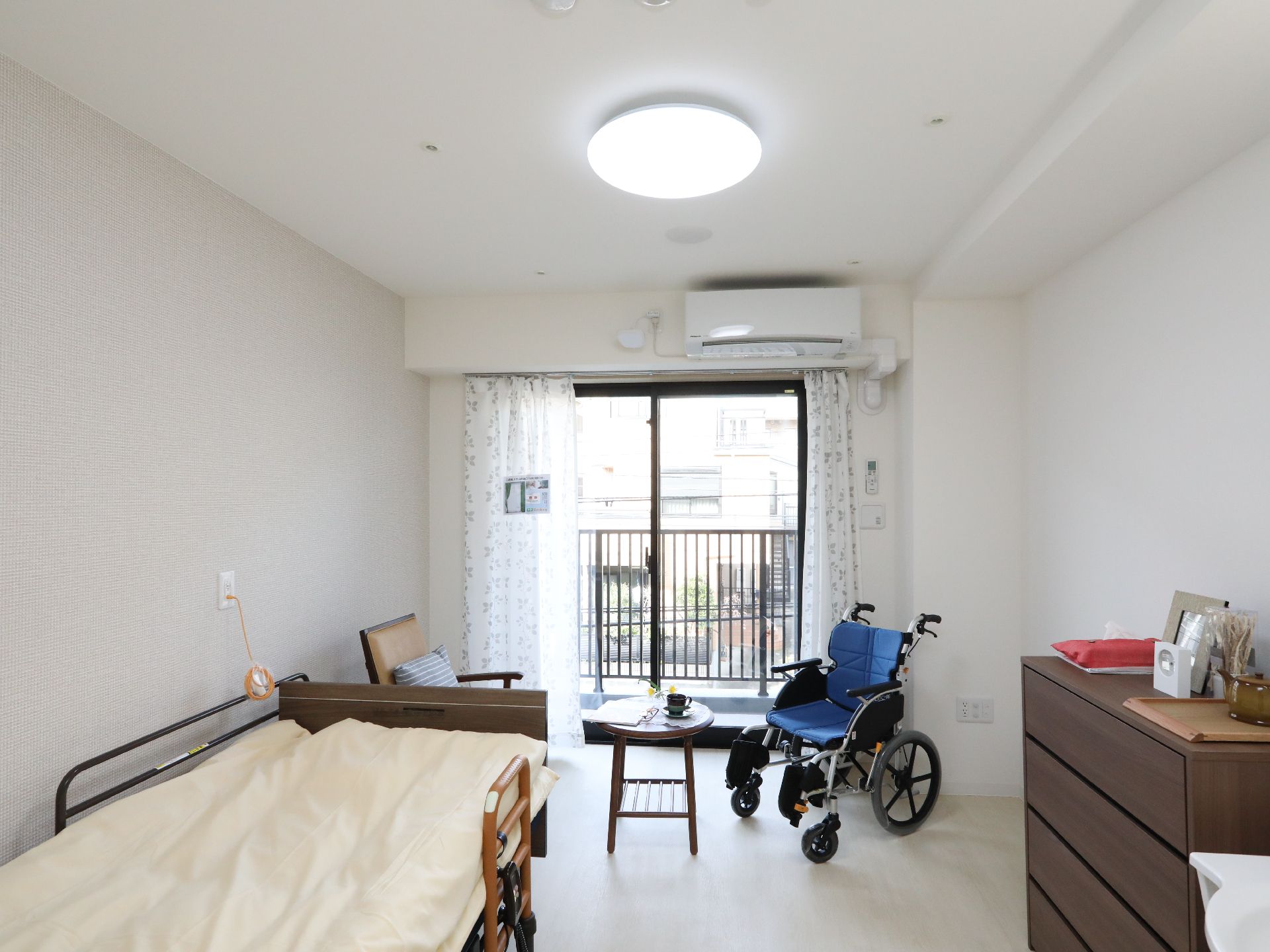 介護用ベッド、チェスト、テーブルが設置された日当たりのよい居室