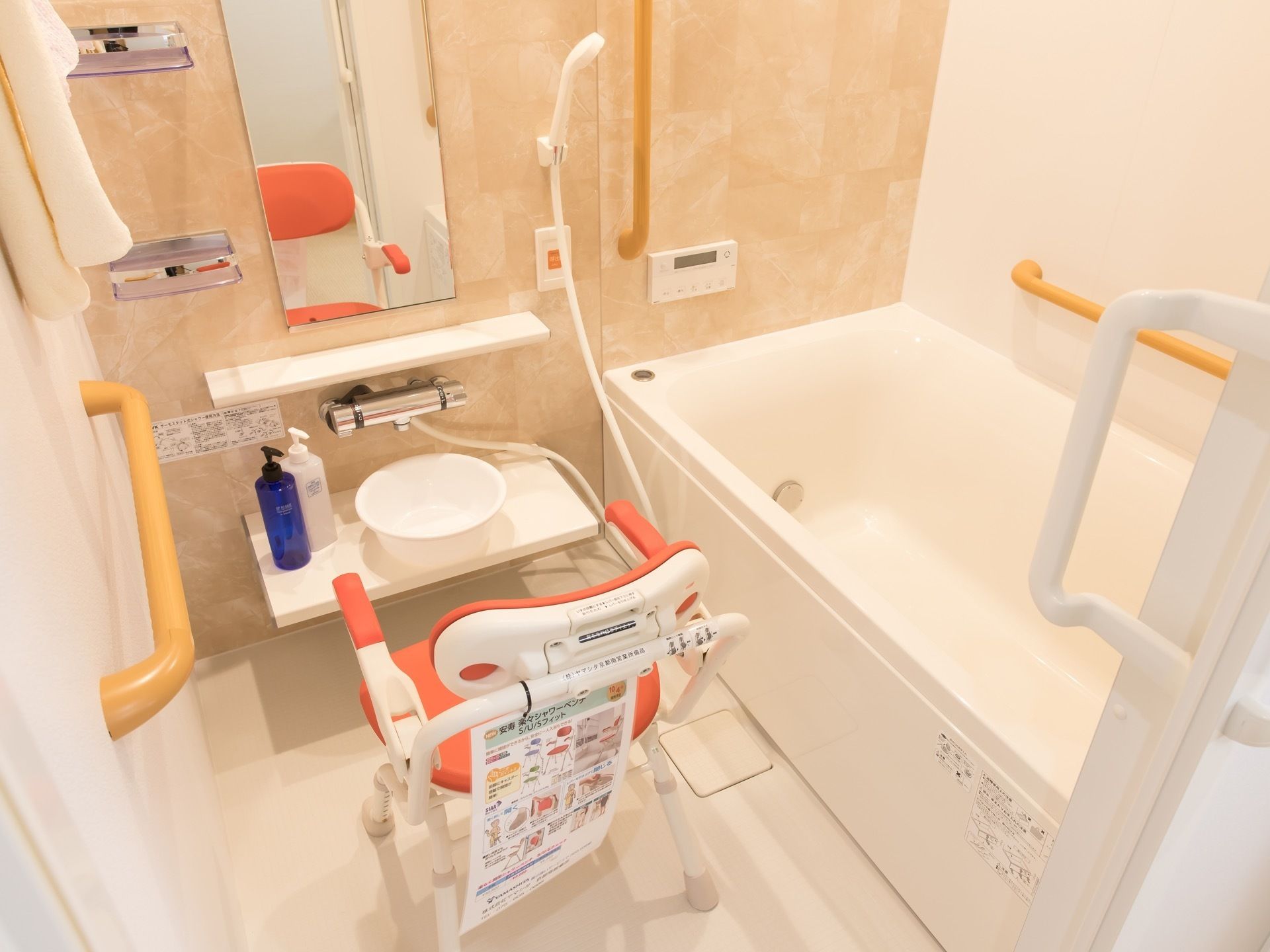 手すりと緊急時用の呼び出しボタンを壁に備え付けた浴室。ひじ掛け付きのシャワーチェアが１つ置かれている。