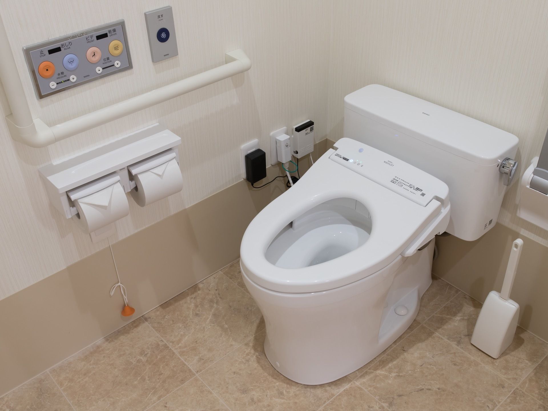 温水洗浄便座付き便器があり、壁にはＬ字型の手すりとトイレットペーパーホルダー、温水洗浄便座の操作パネルなどがある。