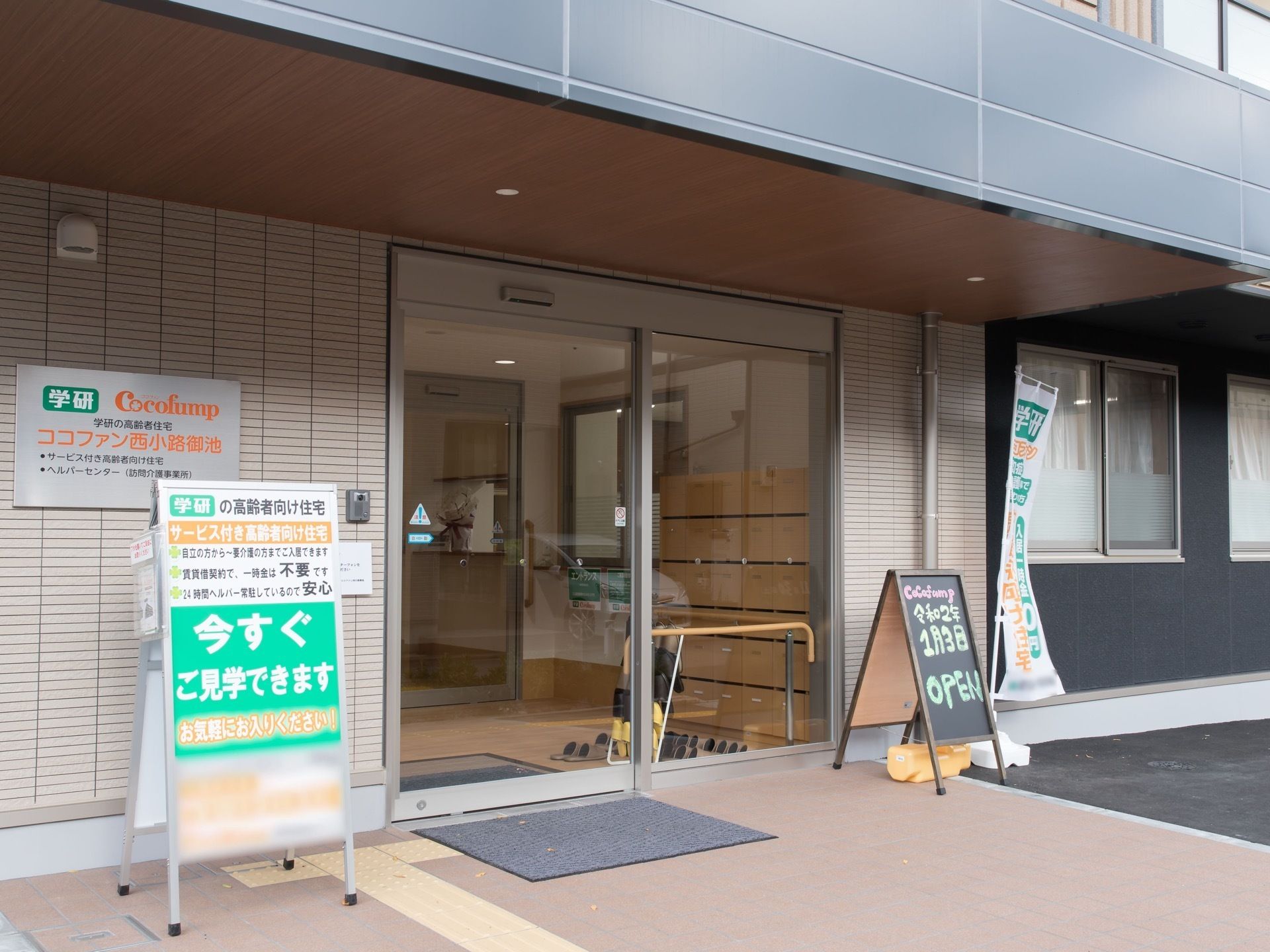 バリアフリーの玄関。床には点字ブロックとグレーの玄関マットがあり、壁や玄関周りには複数の看板も設置されている。
