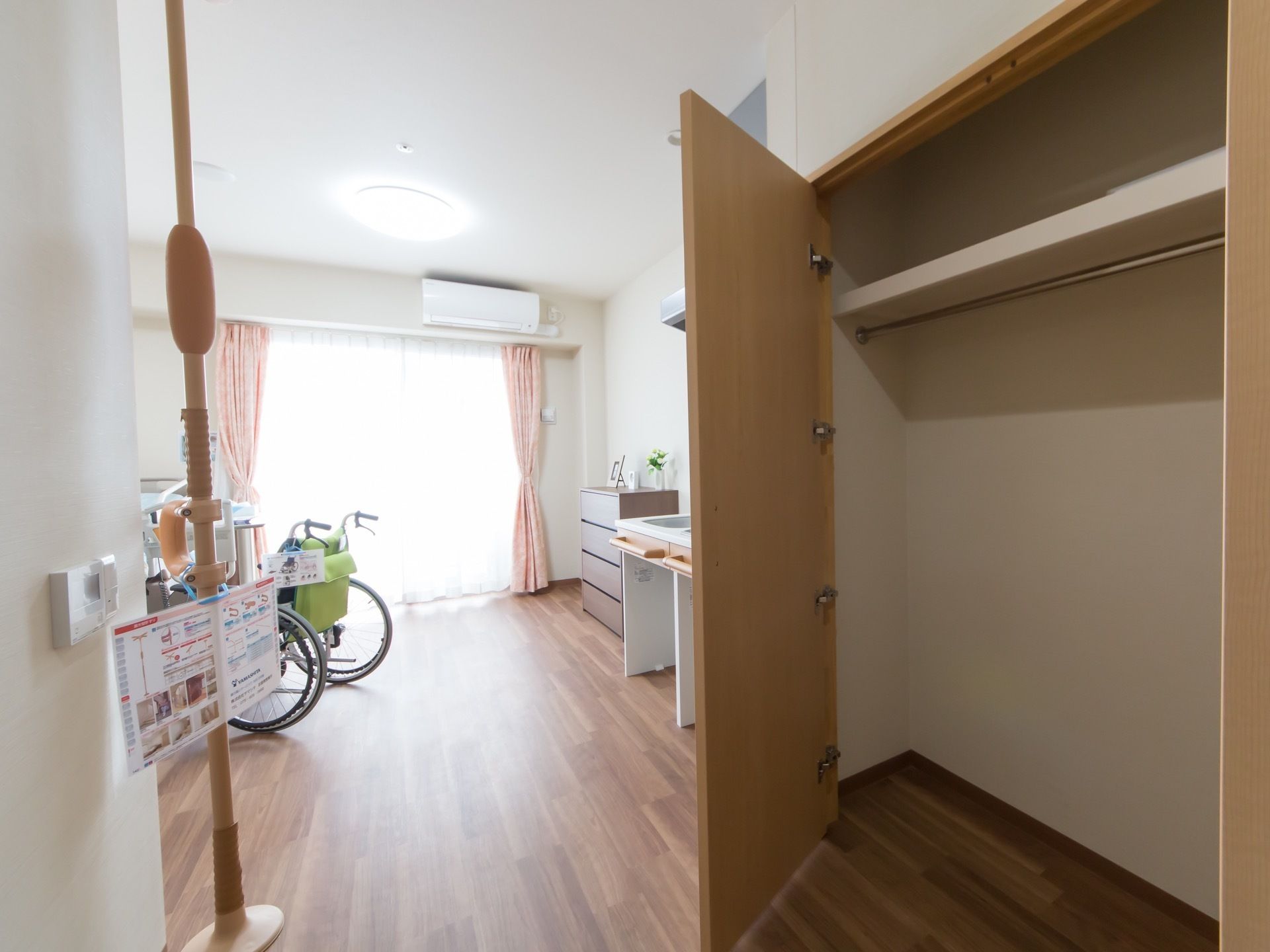 大型の作り付けクローゼットとタンス、キッチンなどがある。掃き出しの大きな窓があり、その上にエアコンも設置されている。