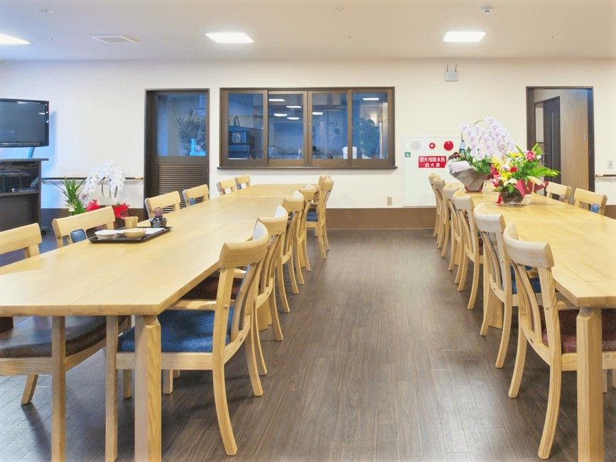 木製の名がテーブルが二つ置かれた食堂。左奥にはテレビや蘭の花がある。