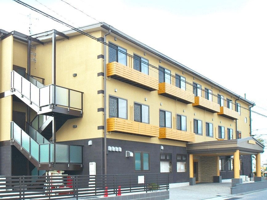 ３階建ての建物はベージュと黒でスタイリッシュな雰囲気。窓が多く、屋外には階段も設置されている。