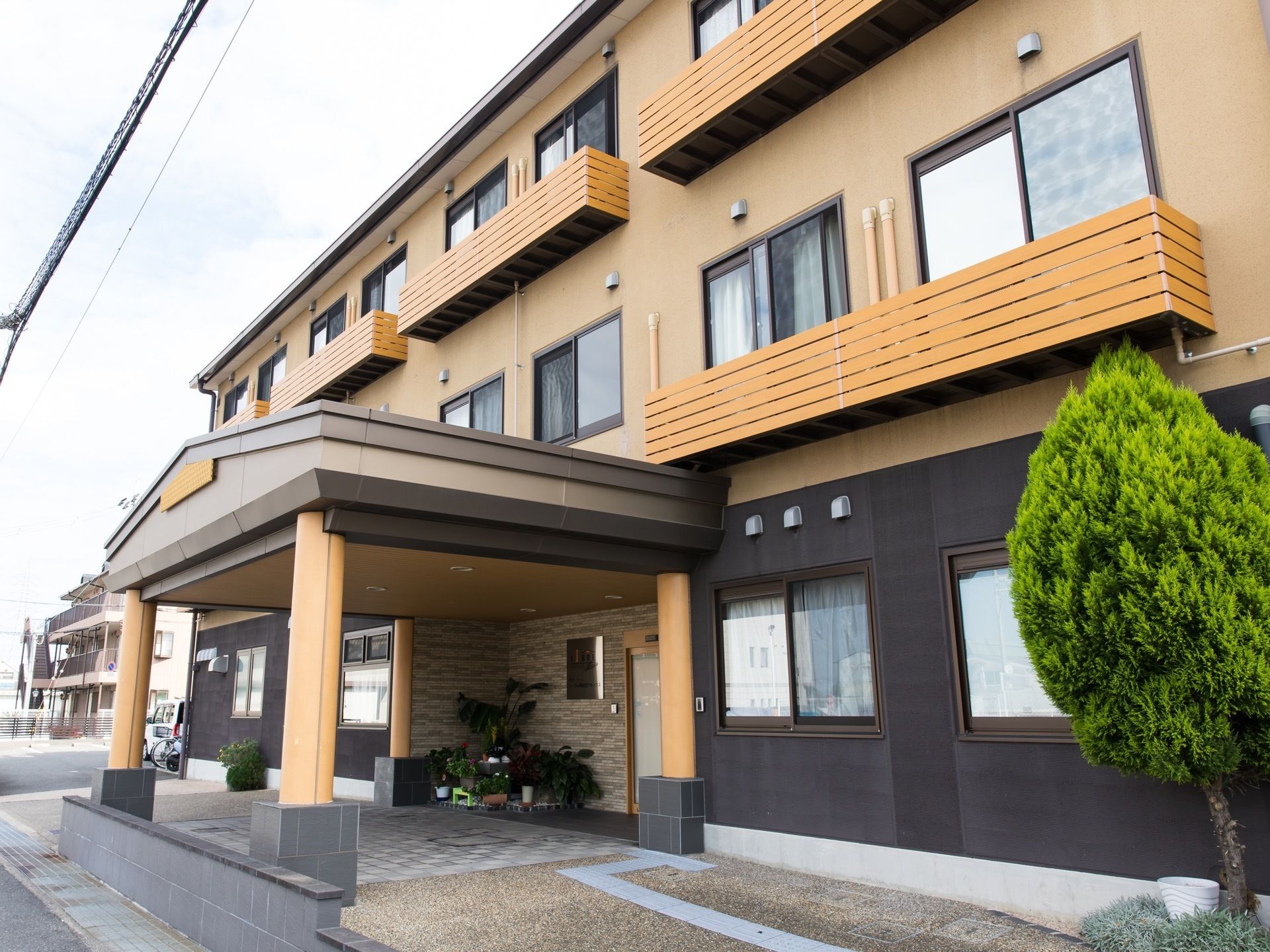 入口には道路に向かって張り出した屋根がある。ドア横は観葉植物の植木鉢が置かれており、緑のある空間ある。