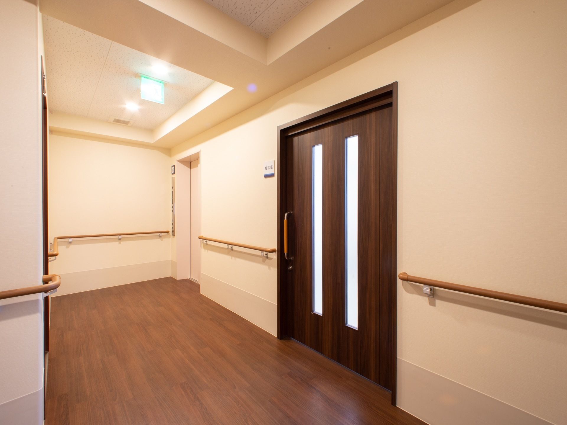 フローリングにシンプルな白い壁の廊下がある。居室の入口は大きな引き戸になっている。壁には手すりがついている。