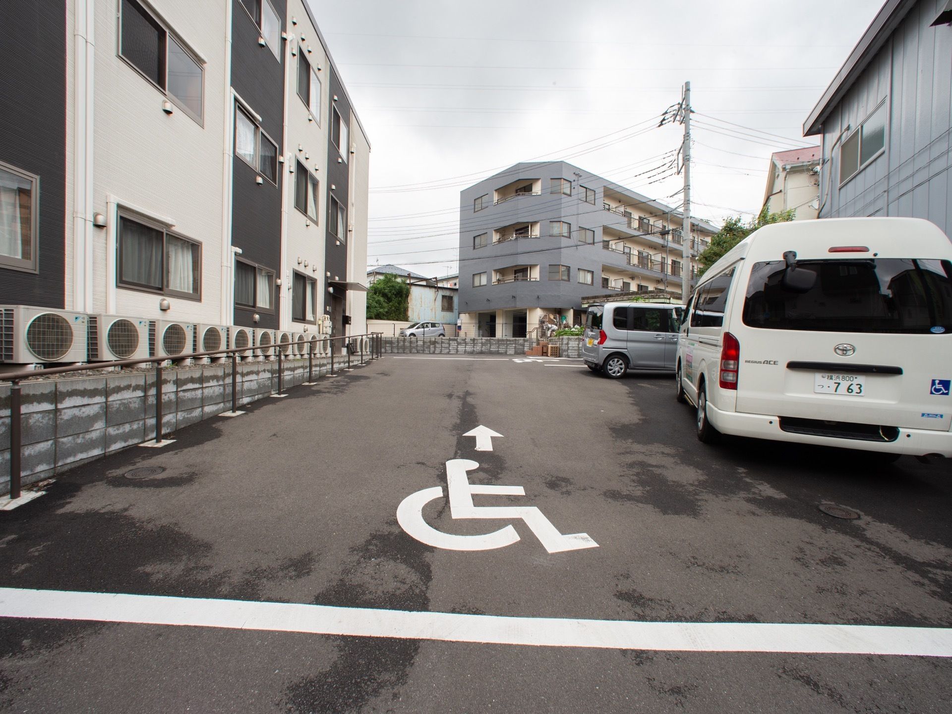 建物の横にアスファルトで舗装された駐車スペースがある。玄関の近くには車椅子対応の車両が停められる場所も設けられている。