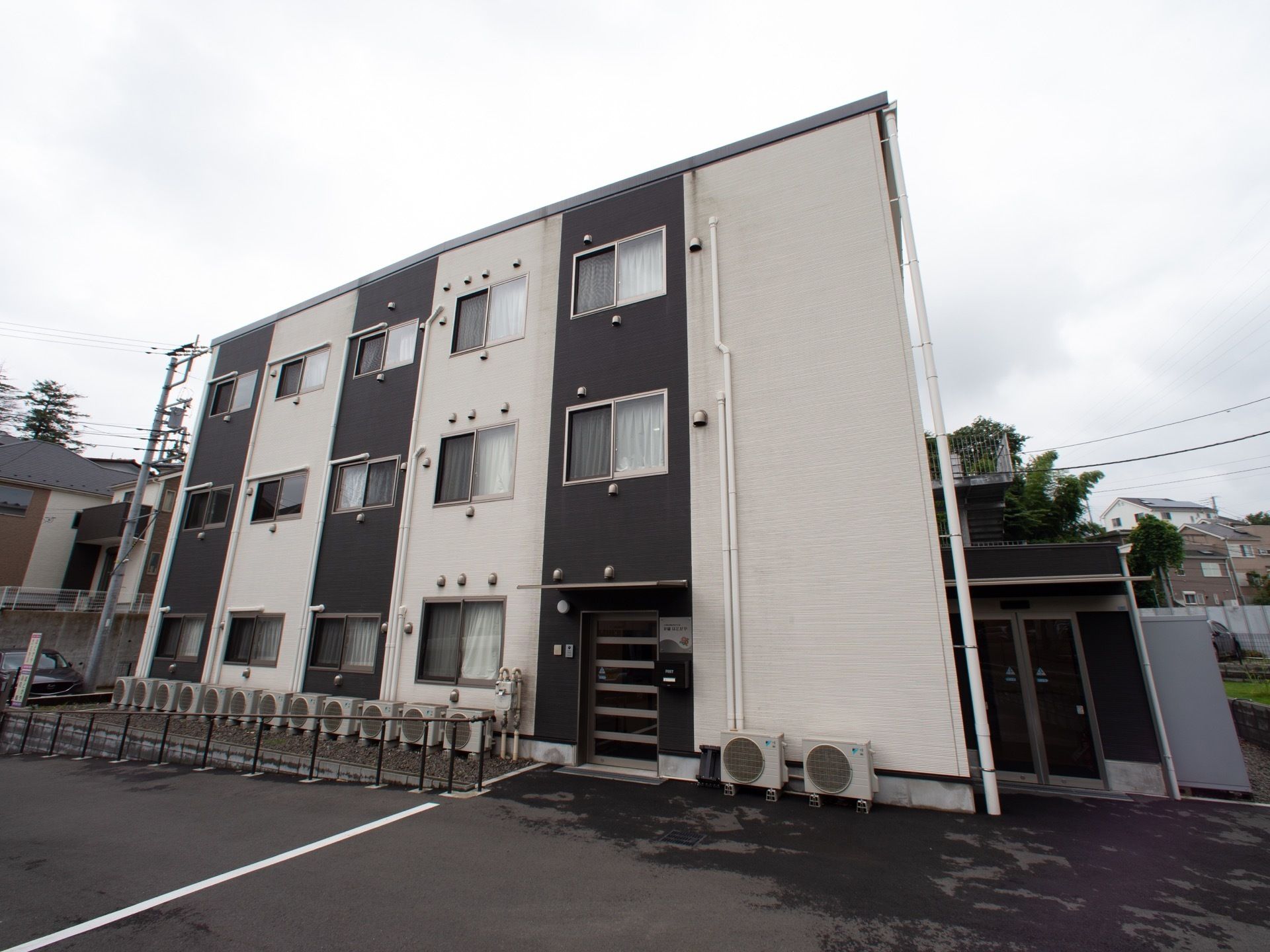 白と黒の２色のパネルで彩られた３階建ての建物がある。玄関までは緩やかな坂になっていて、手すりが設けられている。