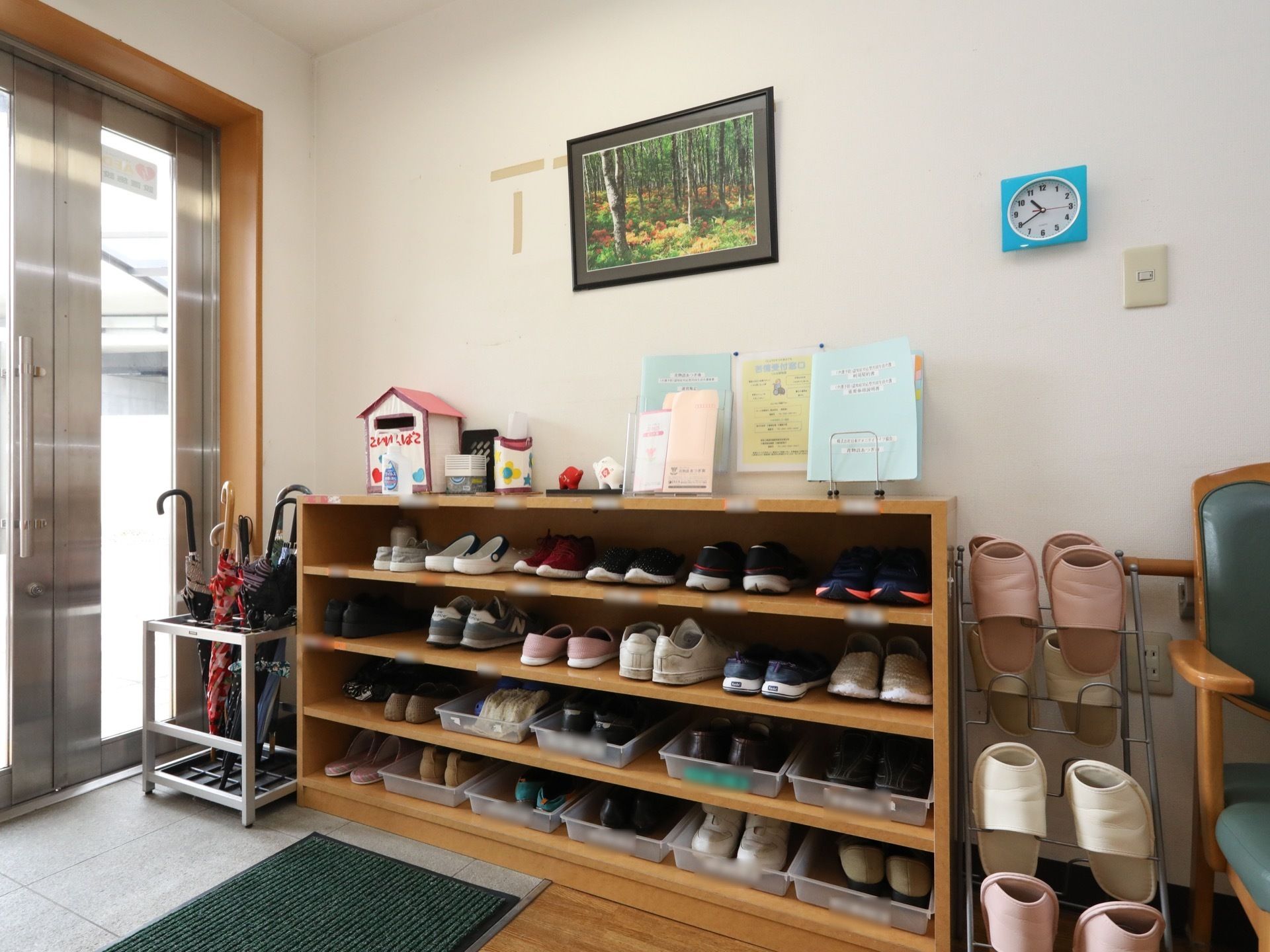 玄関内部に、棚板が３枚ある横長の靴棚が設置されている。その上には、ご意見箱やファイル、案内のチラシが載っている。