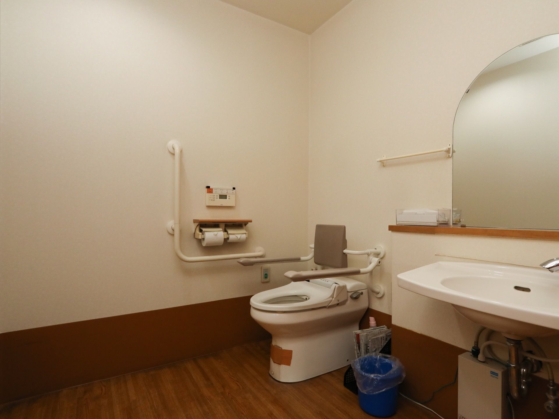 広いスペースに共用トイレが設置されている。便座の周りには、背もたれや可動式の手すりが取り付けられている。