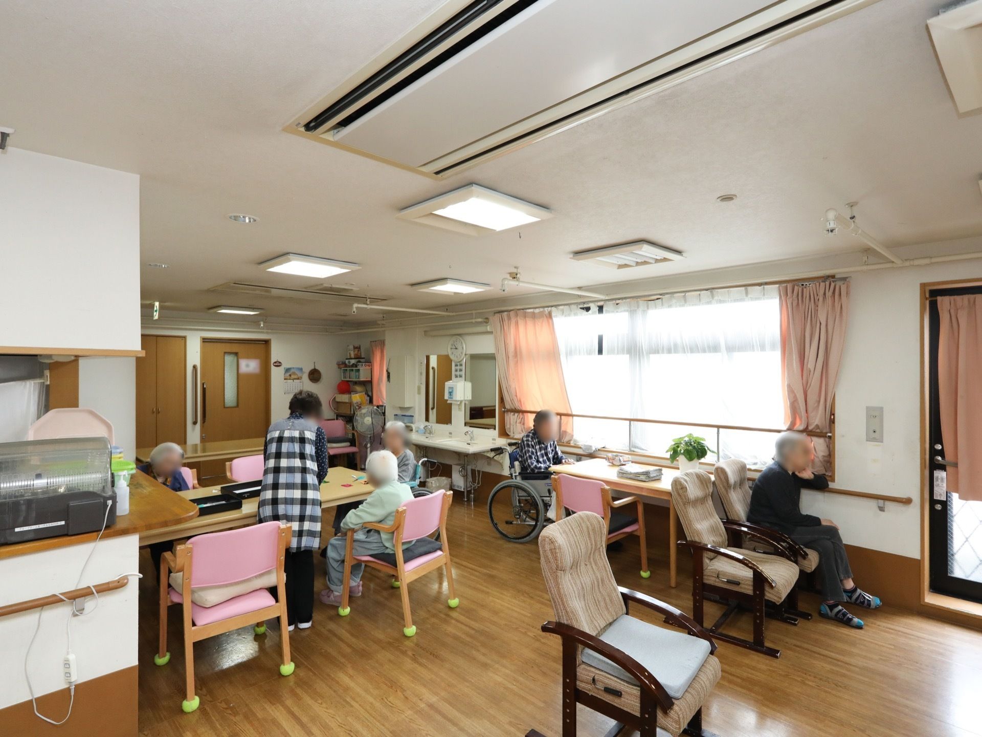 食堂に多くのテーブルと椅子が置かれている。ピンク色の座面や背もたれがついた椅子の脚には、切ったテニスボールがはめられている。