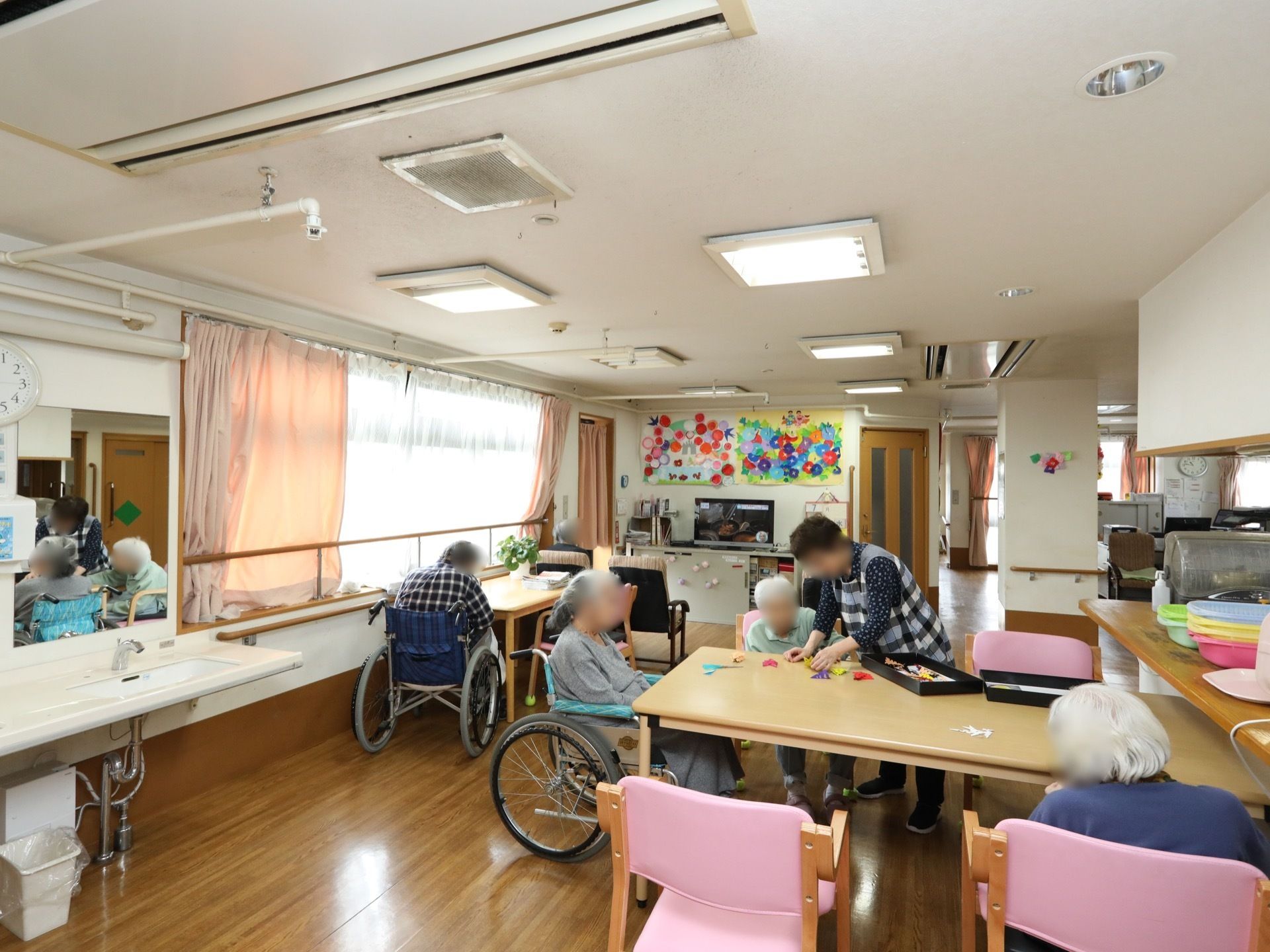 食堂のテーブルのうちの１つに、女性の入居者様が３名集まっている。立っている女性スタッフが創作活動のお手伝いをしている。