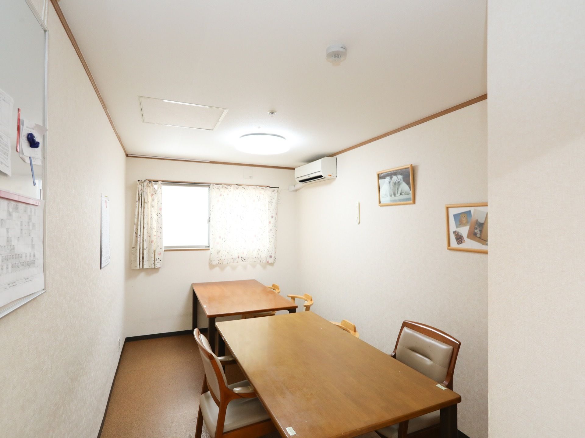 細長の部屋に、テーブルと椅子が設置されている。横壁に、絵画、エアコンがある。手前の壁に、ホワイトボードが掛けられている。