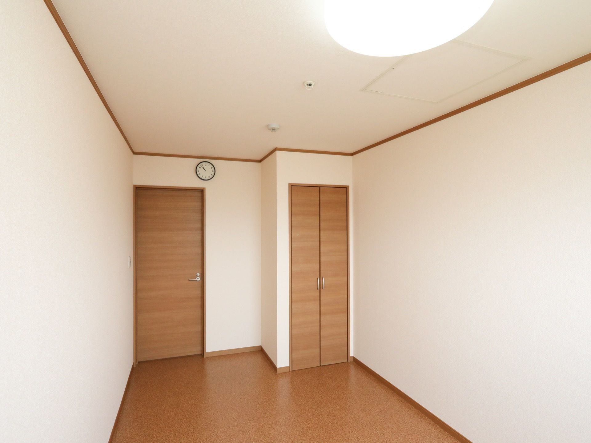 居室内の床は、モダンな感じの色合いのタイルカーペットとなっている。天井と壁は白で統一されている。天井照明は丸くて大きいものが付いている。