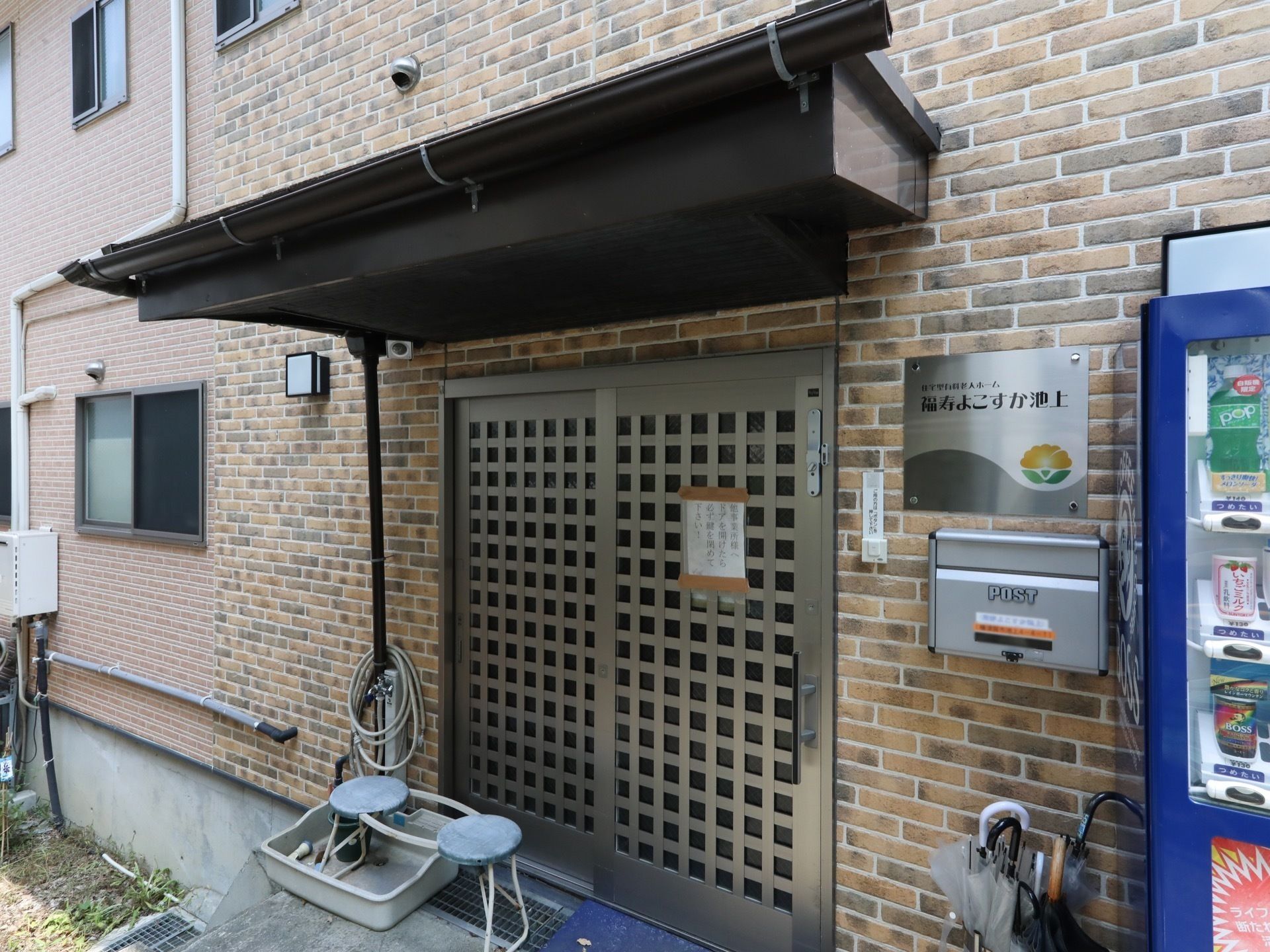 近くに自動販売機が設置されている屋根付きの高齢者施設の玄関