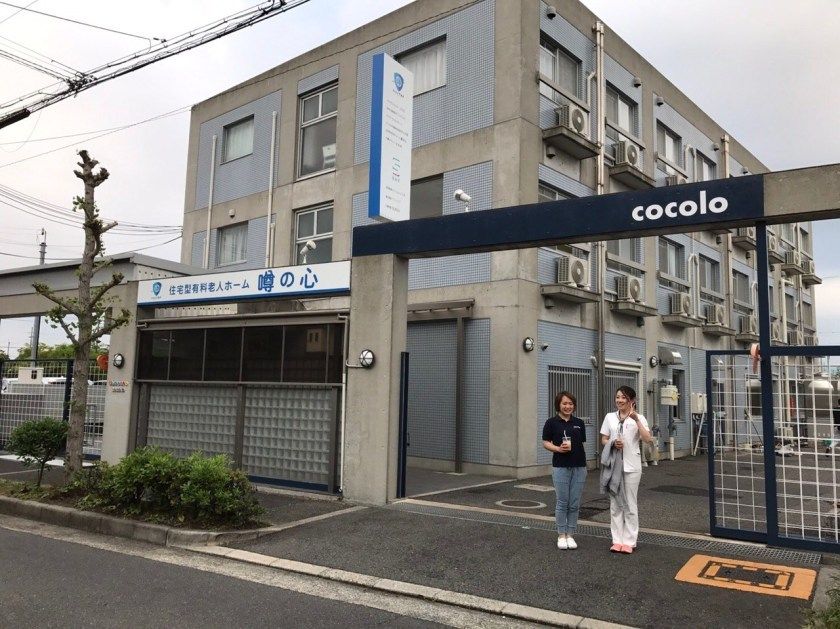 3階建ての建物はグレーを基調としたしっかりとした造り。建物の前に2名の女性が立っている。