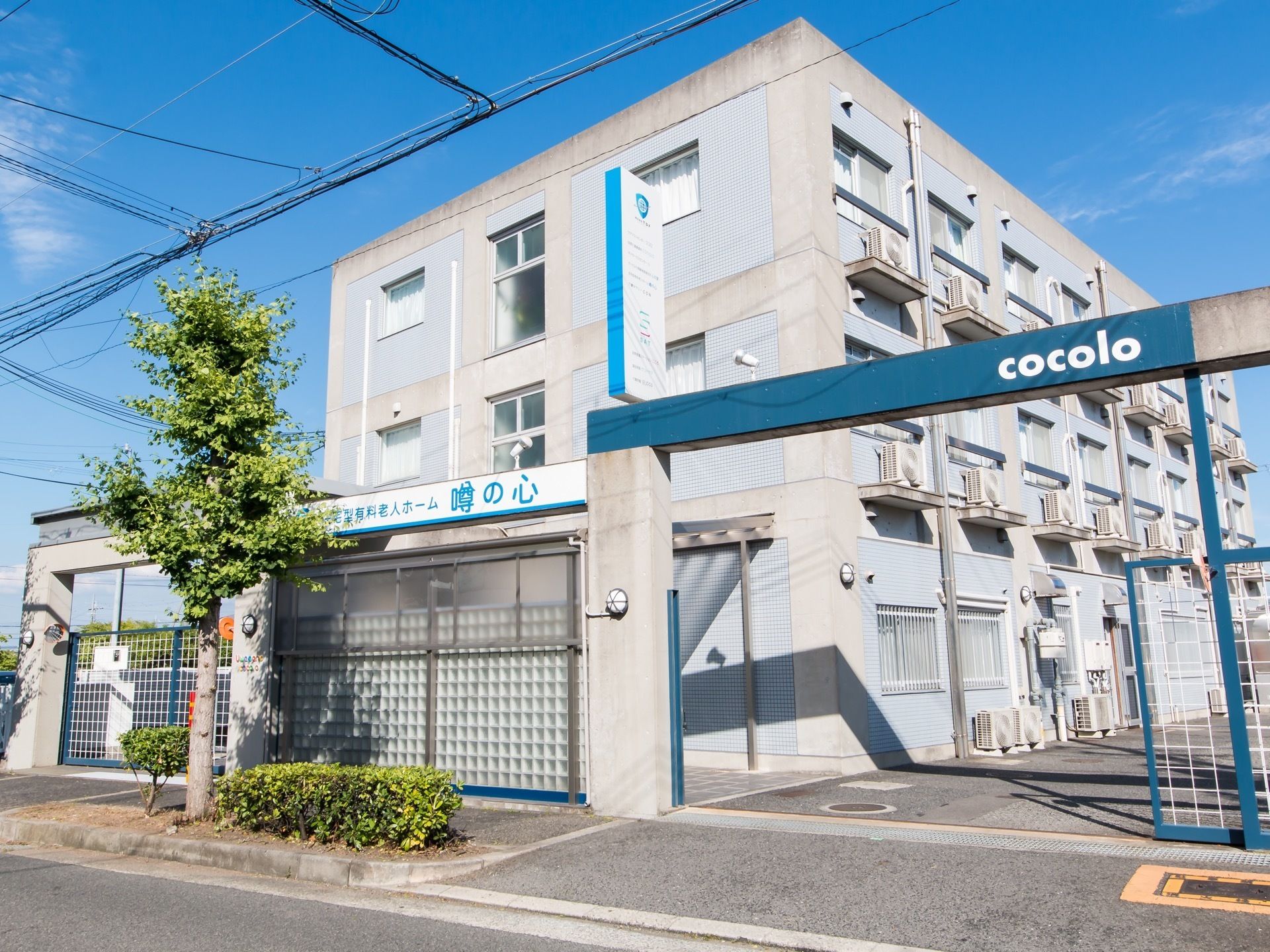 外壁はコンクリートを打ちっぱなしにしたおしゃれなデザインである。３階建ての施設出入口にゲートが取り付けられている。