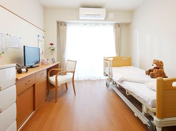エアコンやデスクセット、ベッドが置かれた居室には花やぬいぐるみも飾られている。