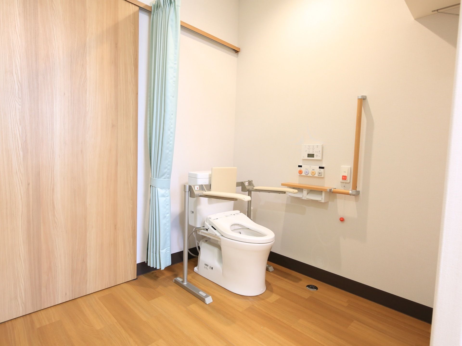 居室に入ってすぐの所に、トイレが設置されている。水色のカーテンで仕切れるようになっている。