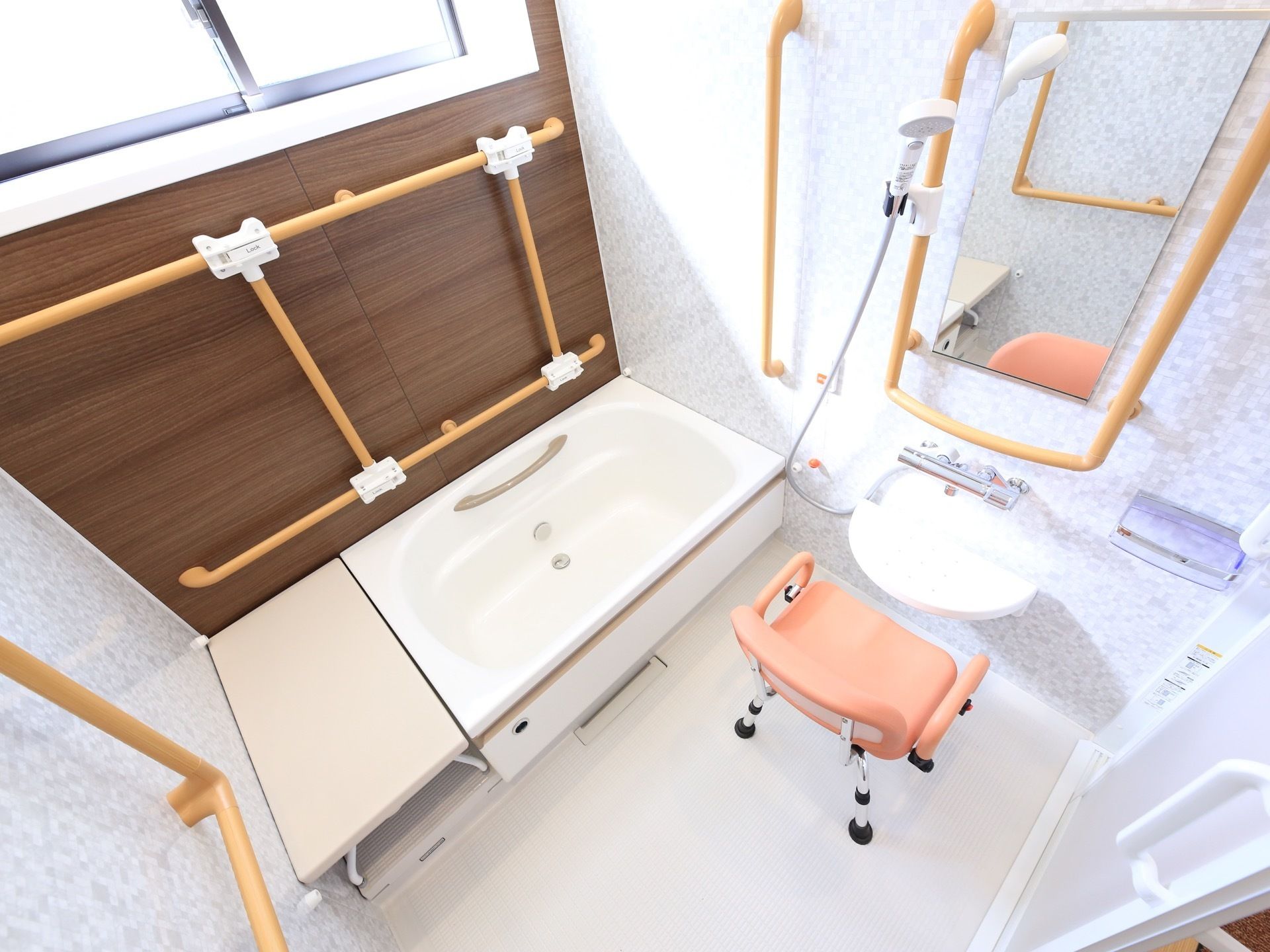 薄いオレンジ色の座面やひじ掛けがついた椅子が洗い場に置かれている。薄い茶色の手すりがいろいろな所に取り付けられている。