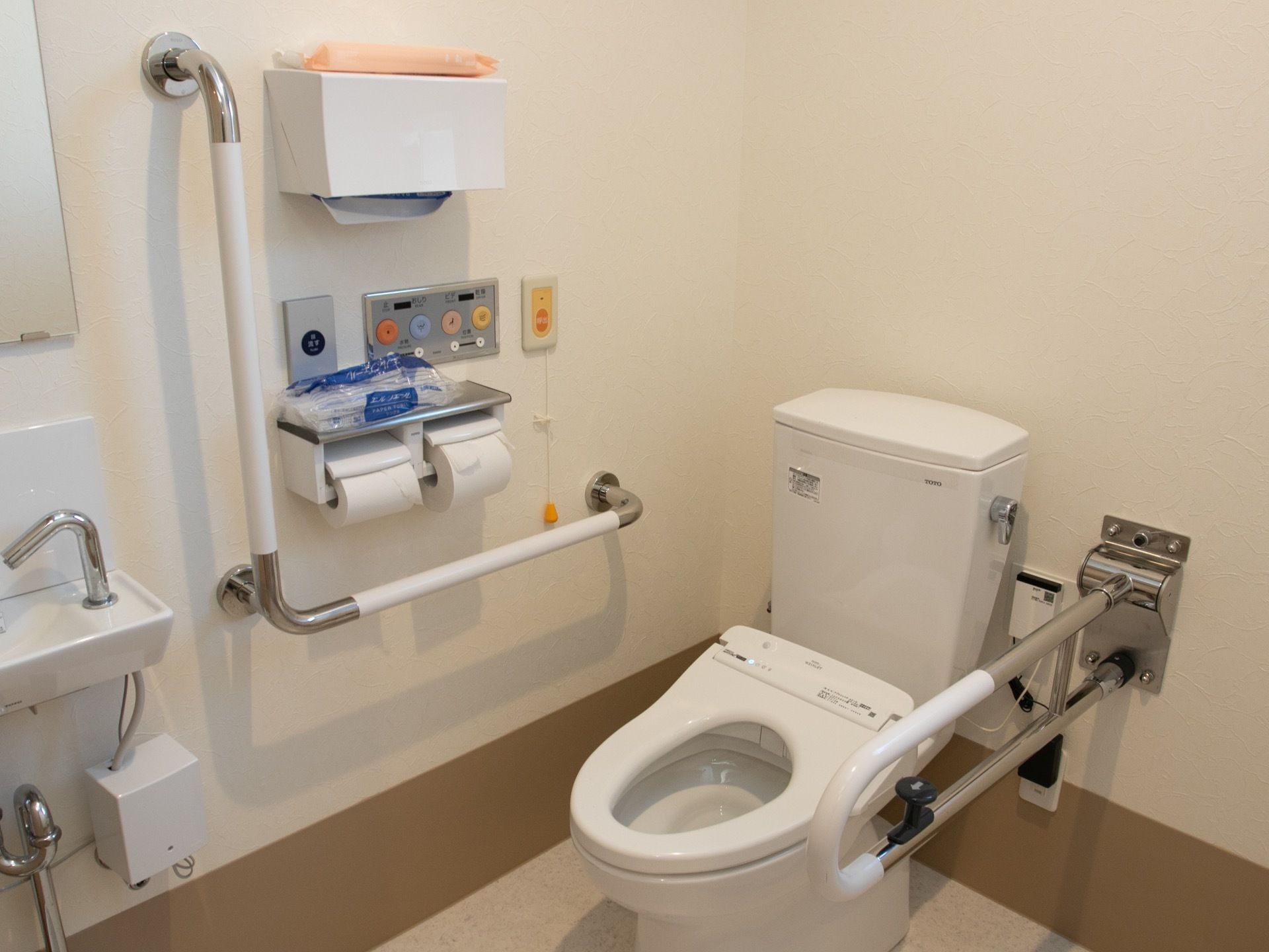 温水洗浄便座器やセンサー付き手洗い場が完備されたトイレである。壁には、可動式手すりやL字型手すりがある。