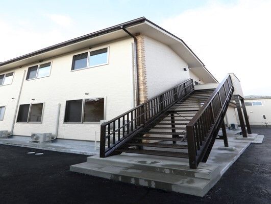 屋外階段が設置されたベージュ系の２階建ての建物。階段には手すりが付いている。