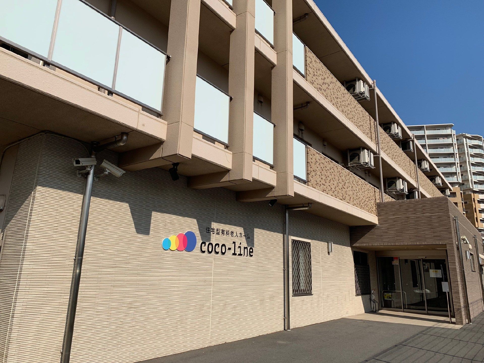 ブラウン系の3階建ての建物。各フロアにベランダが付き、周辺には背の高いマンションなどの住宅がたくさんある。