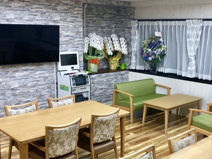 大きなテレビがある食堂にはグリーンの応接セットやダイニングテーブルが複数置かれている。