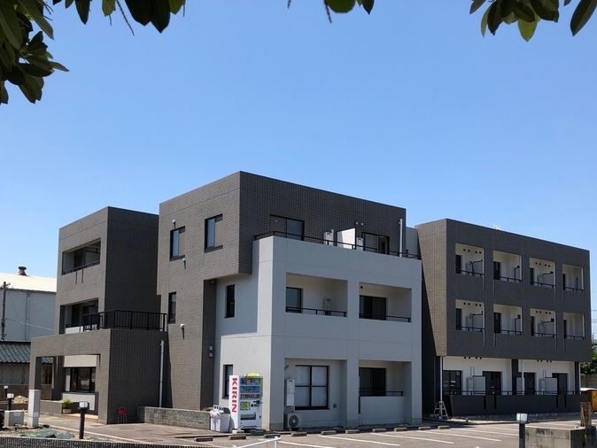 白とダークブラウンの３階建てで日当たりのいい場所に建っている。建物の前には自動販売機も設置されている。