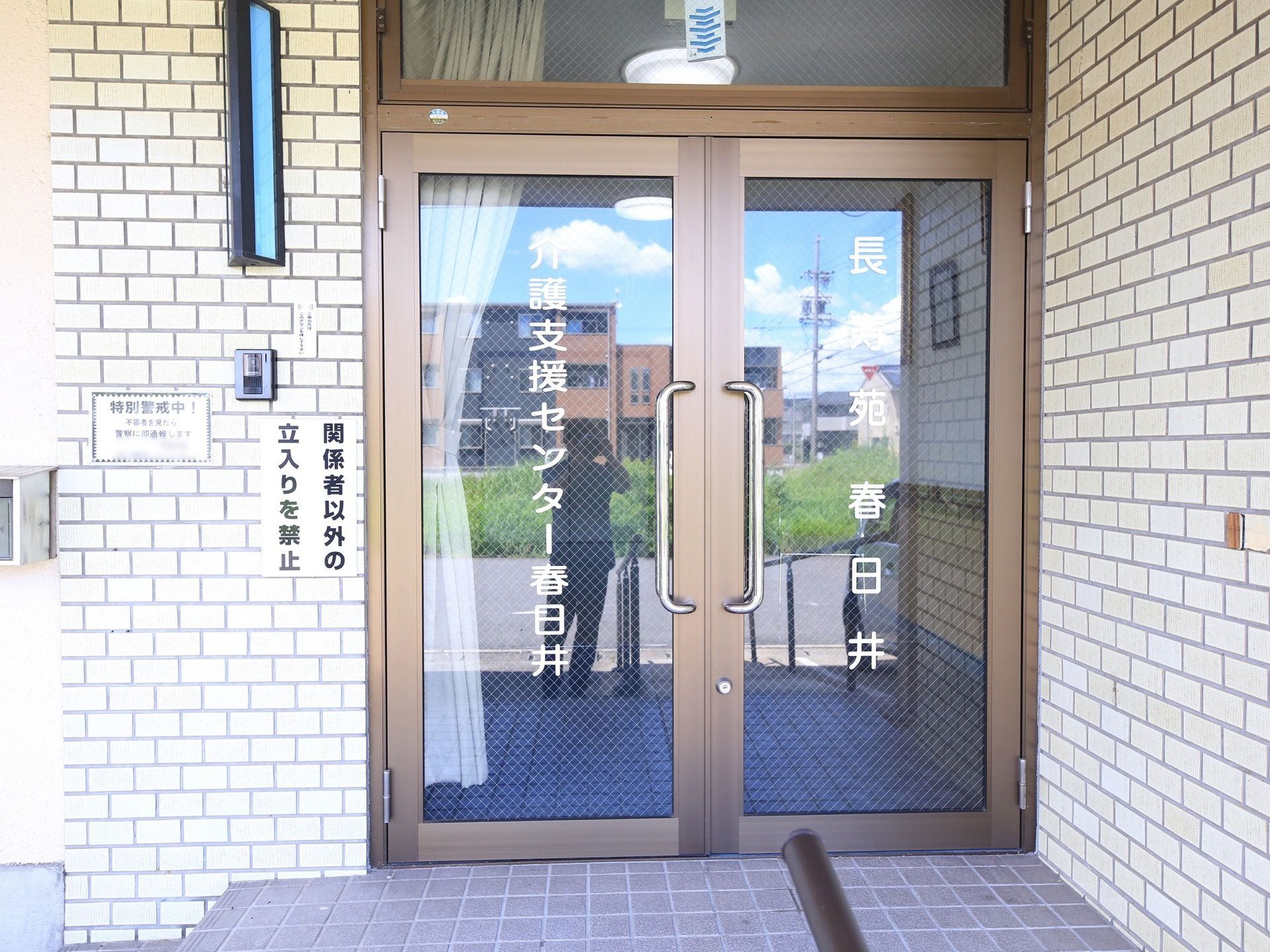 階段と手すり付きのスロープが玄関まで続いている。扉は観音開きの大きなガラス戸で、反対側がよく見通せる。