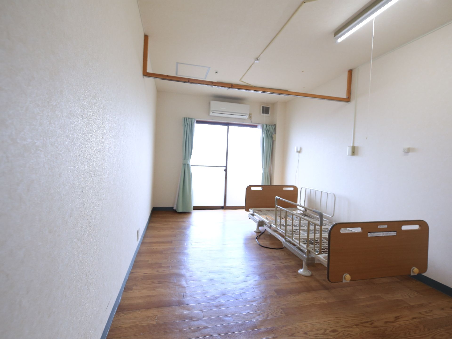 介護用ベッドとエアコンが設置された天井の高い居室空間