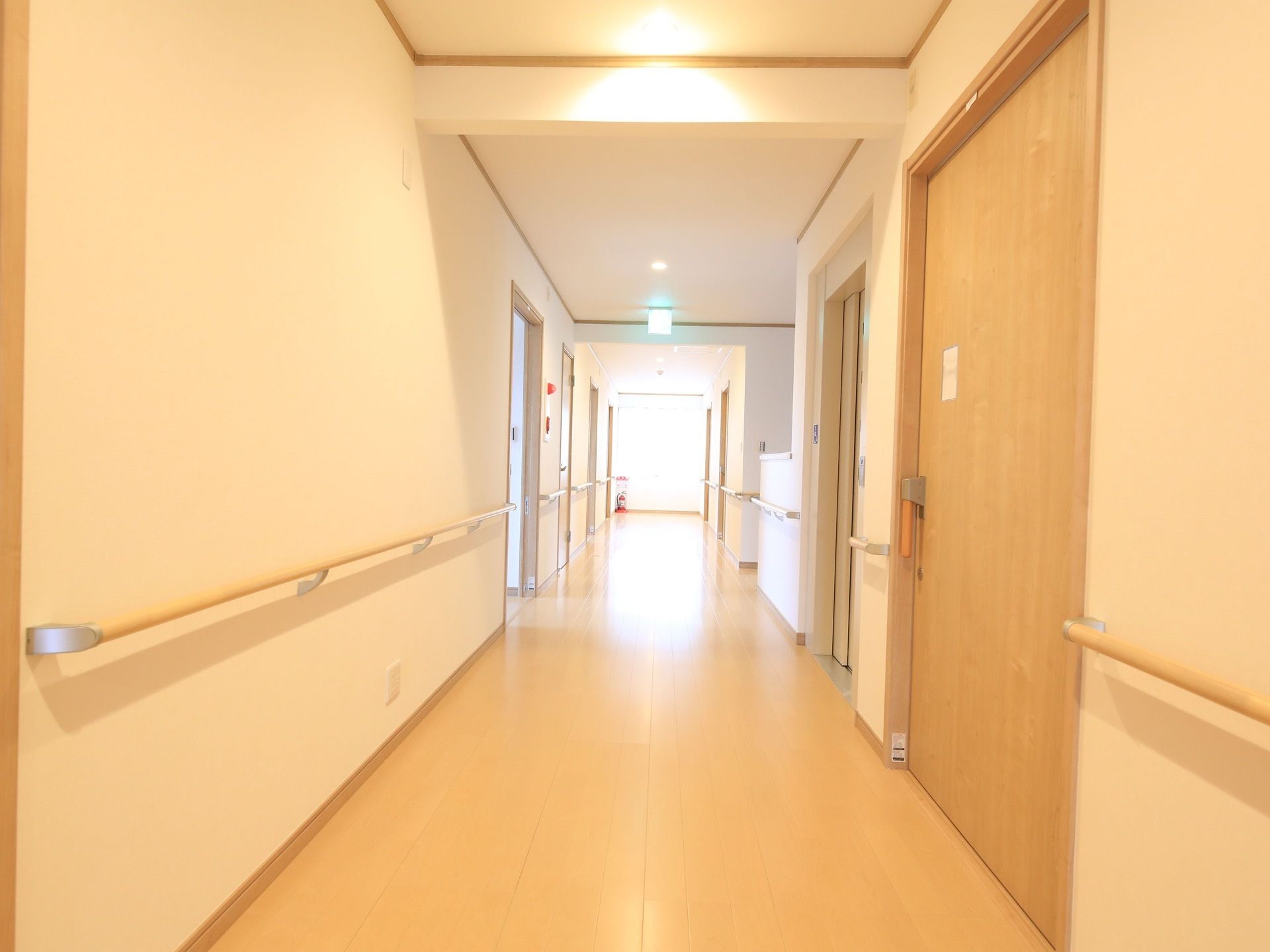 見通しのよい直線の居室前の廊下には、両サイドの壁に手すりが設置され、温かみある色合いの照明が点いている。