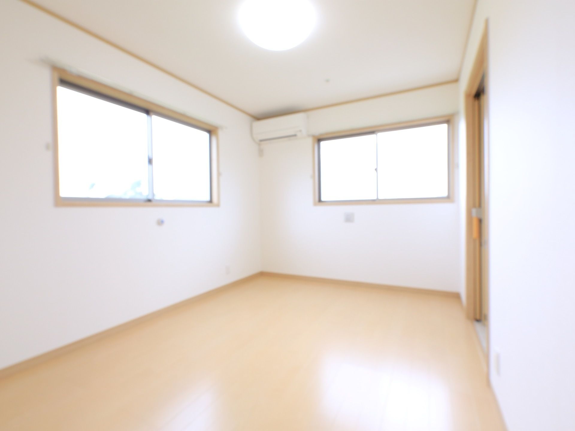 居室は、天井と壁面が真っ白で、床面は白木色のフローリングである。２壁面に窓があり、壁面上部にエアコンがある。