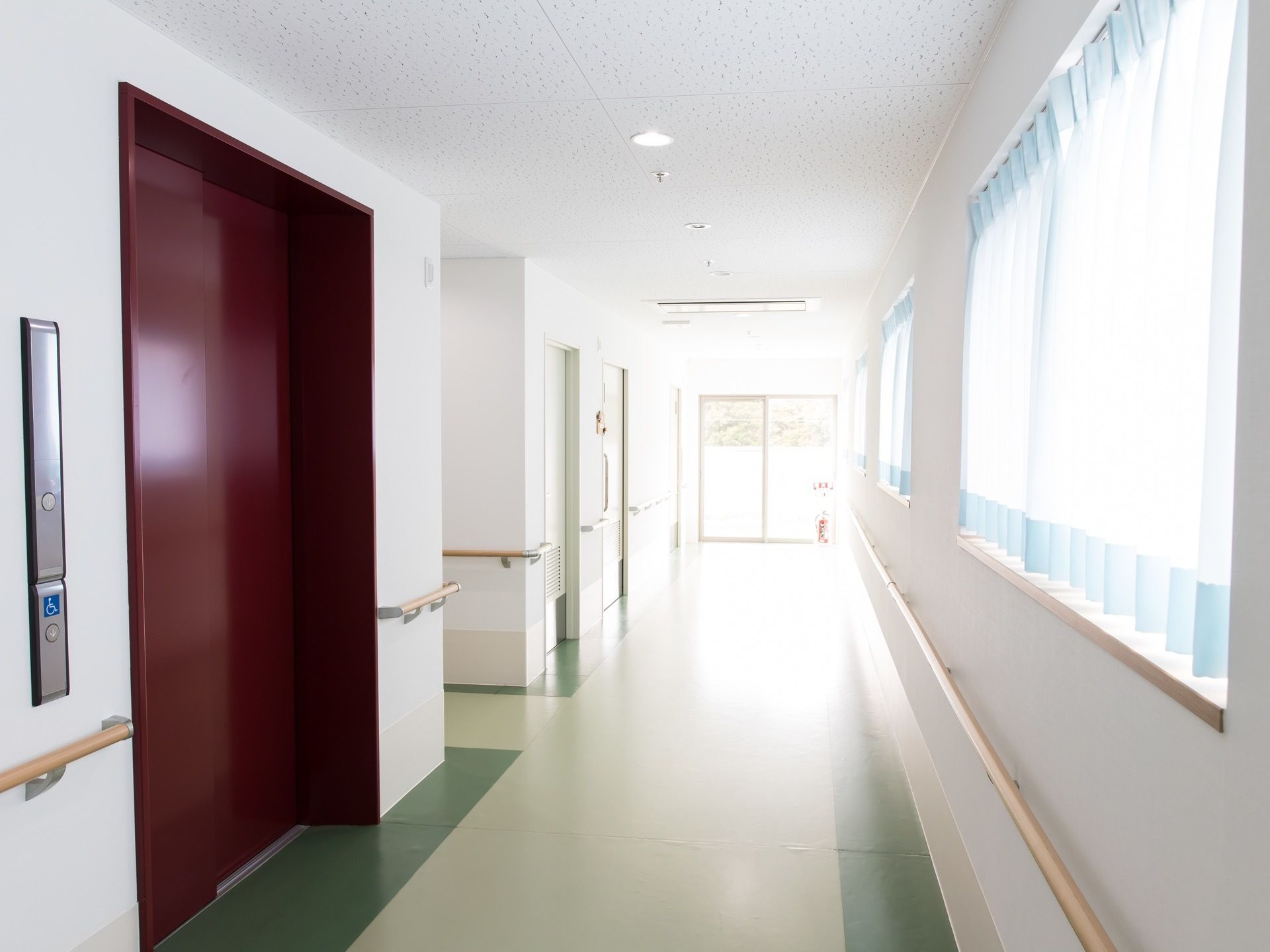 窓から外光が入る廊下になっている。手すりが壁全面に設置されており体を支えることができる。エレベーターがある。