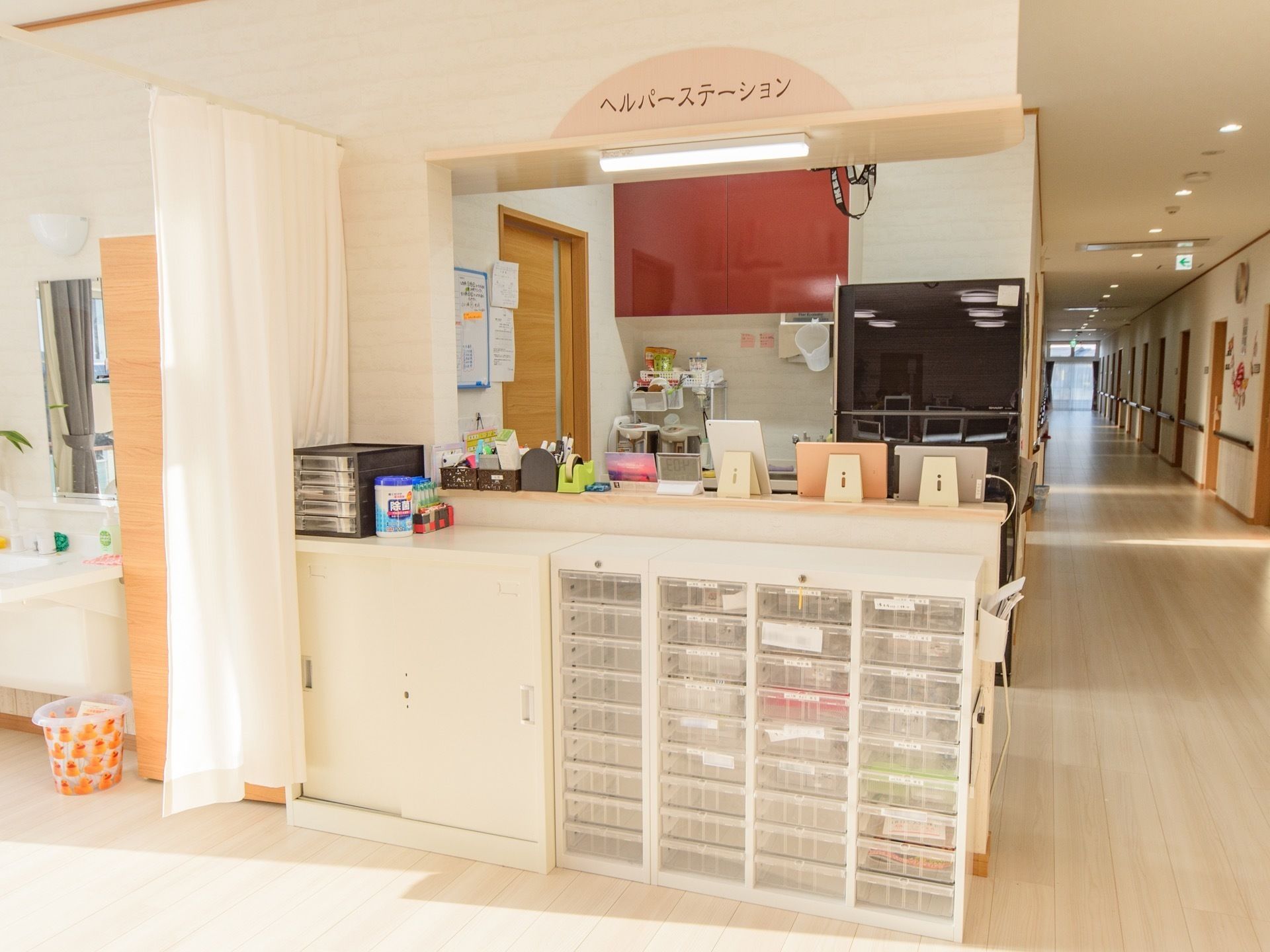 長く続く廊下の手前にヘルパーステーションと書かれた受付がある。カウンター前にはたくさんの引き出しが付いた書類ケースが並んでいる。