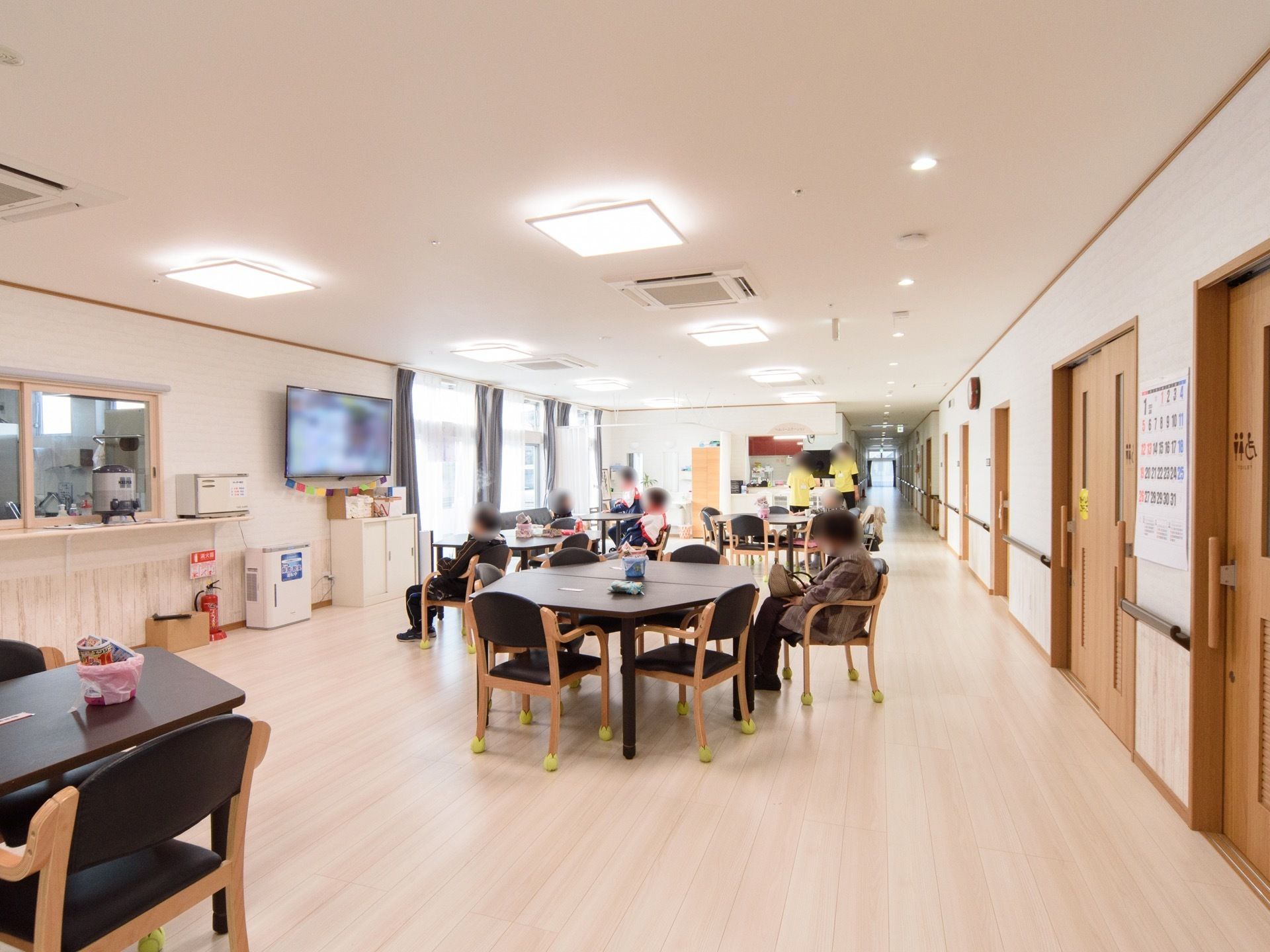 食堂兼リビングの壁に、大きなテレビが掛かっている。入居者様数人が、テレビを見ていたり、くつろいだりしている。