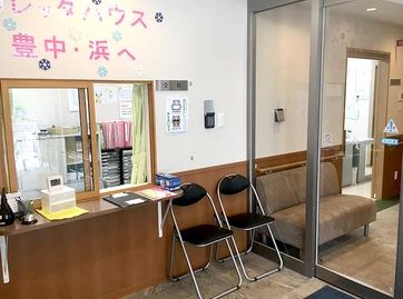 緑の多い屋外で笑顔で過ごしている車いすの高齢女性とエプロンを付けた男性スタッフ。