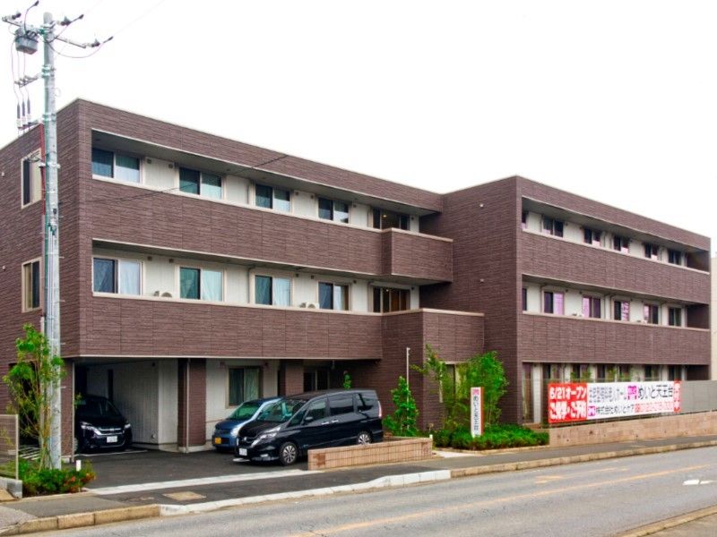 焦げ茶色の壁の建物。3階建てで1階に駐車場がある