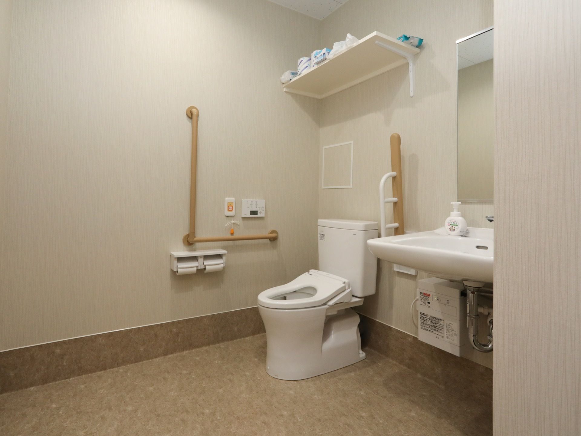 ゆとりあるスペースが確保されたトイレである。温水洗浄便座や洗面台が完備され、壁には手すりが設置されている。