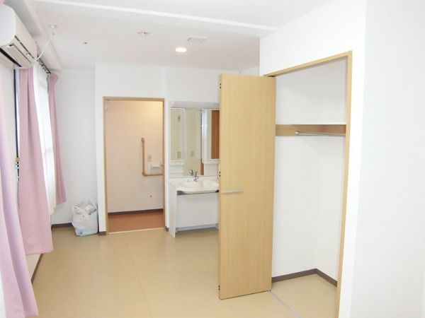 エアコンを挟んで２か所に窓がある広めの居住空間。奥のほうにトイレと洗面台がある様子