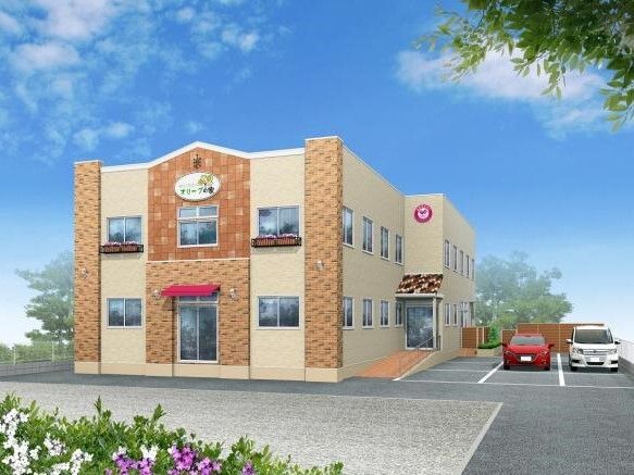外壁には住宅名も書かれている２階建ての建物はベージュ系。敷地内には駐車場があり、車が止まっている。